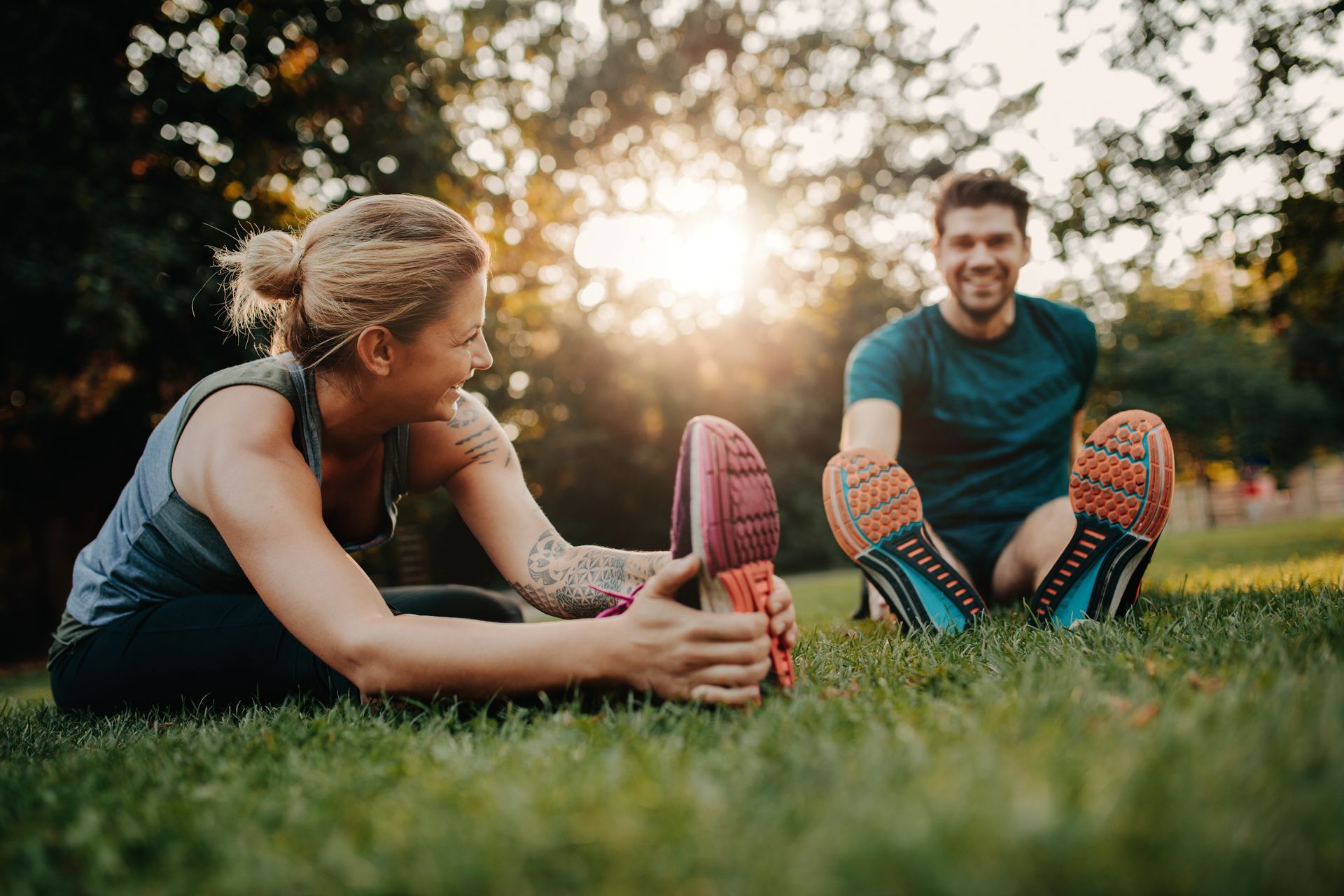 A man and a woman are sitting on the grass stretching their legs.