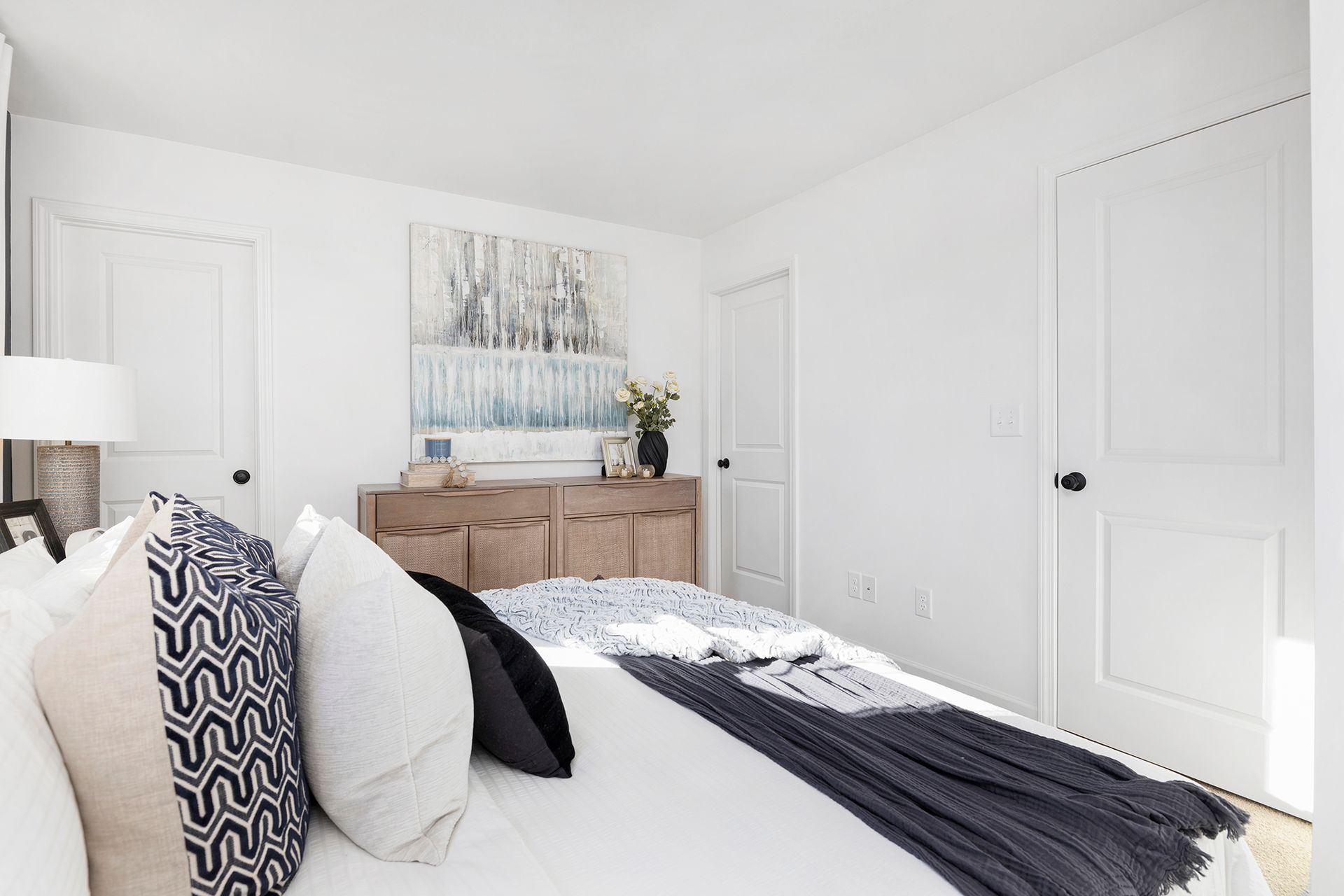 A bedroom with a bed , dresser , lamp and painting on the wall.
