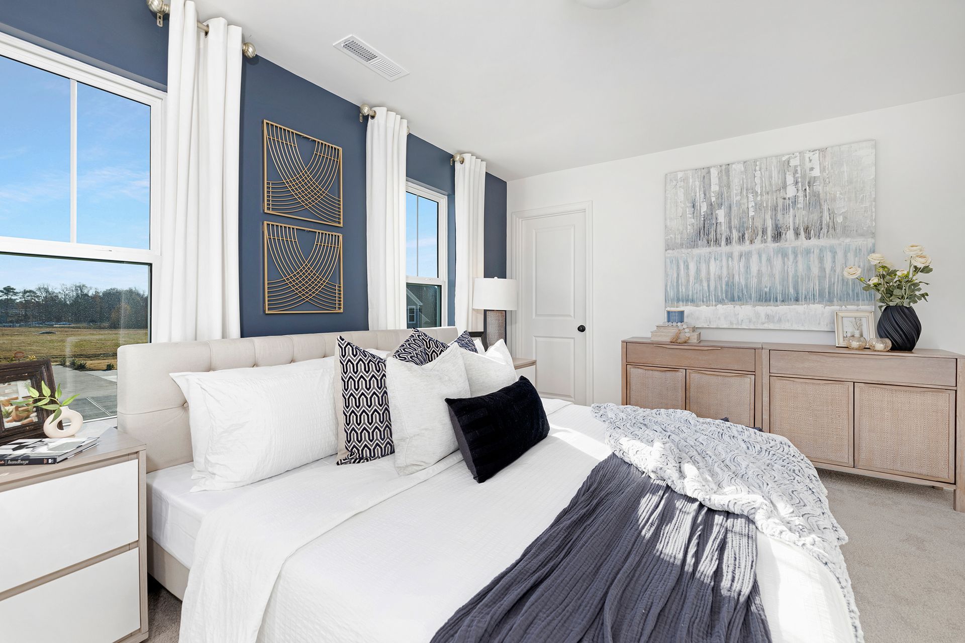 A bedroom with a large bed , dresser , nightstand and windows.