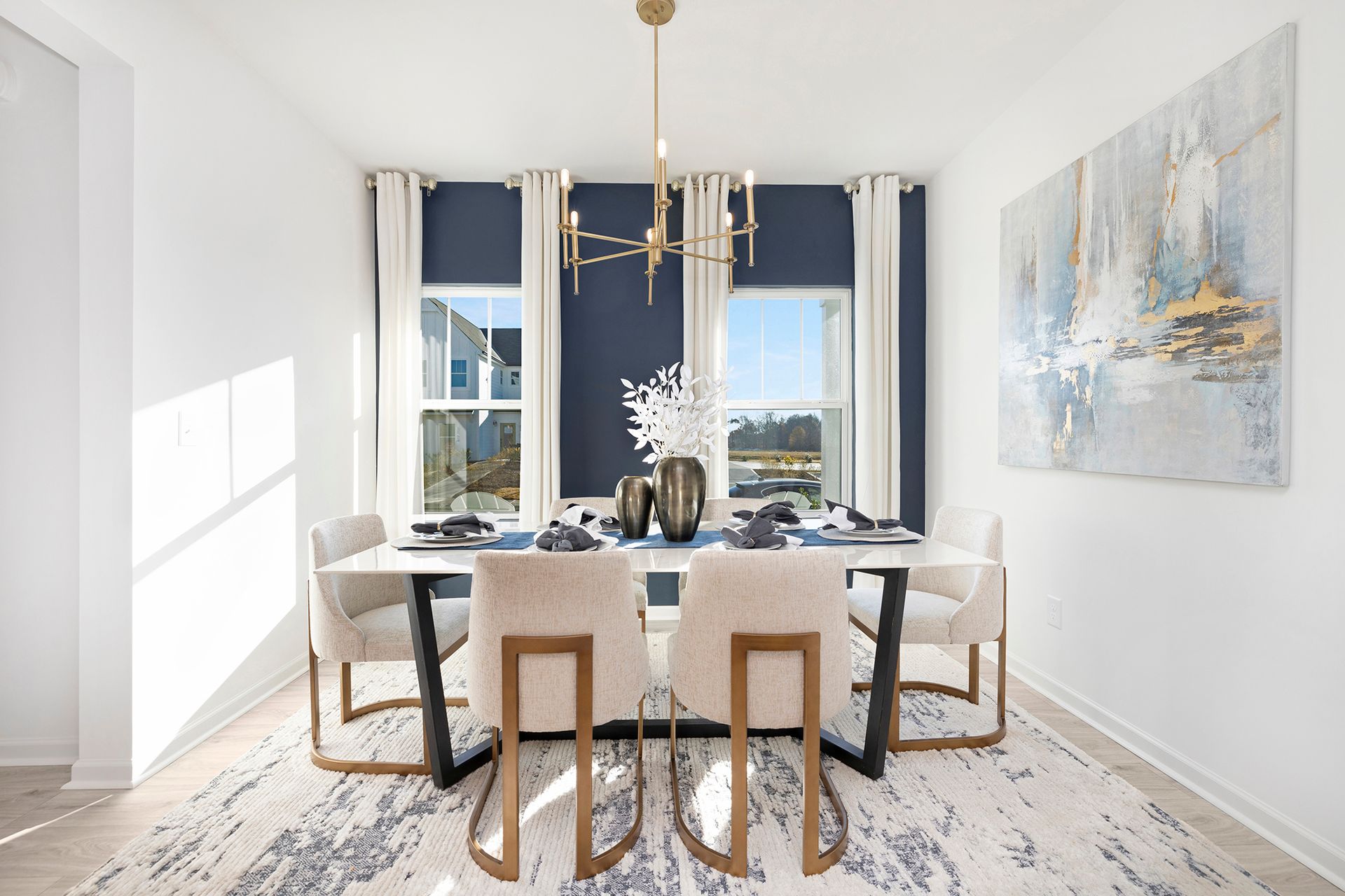 A dining room with a table and chairs and a painting on the wall.