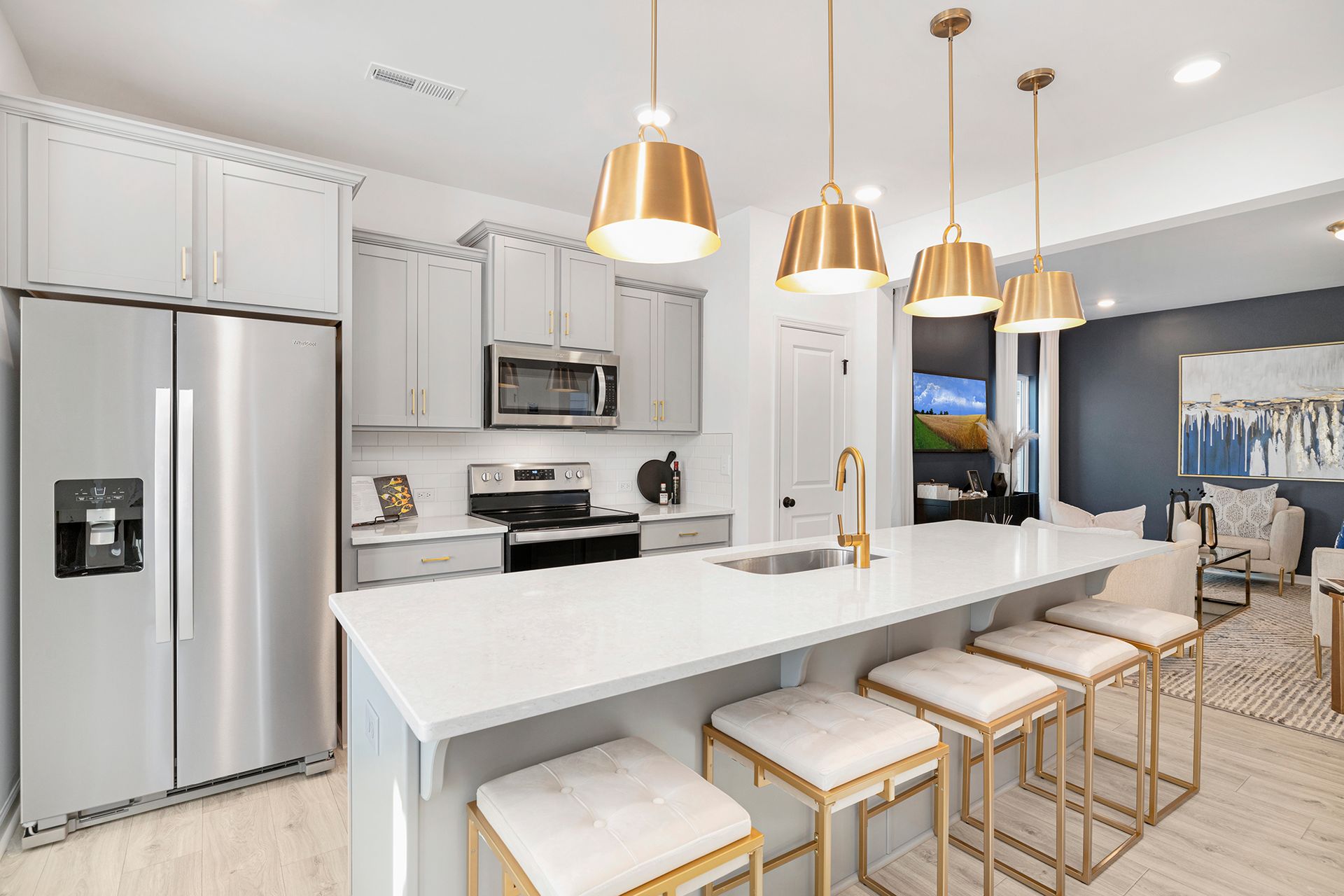A kitchen with white cabinets , stainless steel appliances , a large island with stools and a refrigerator.