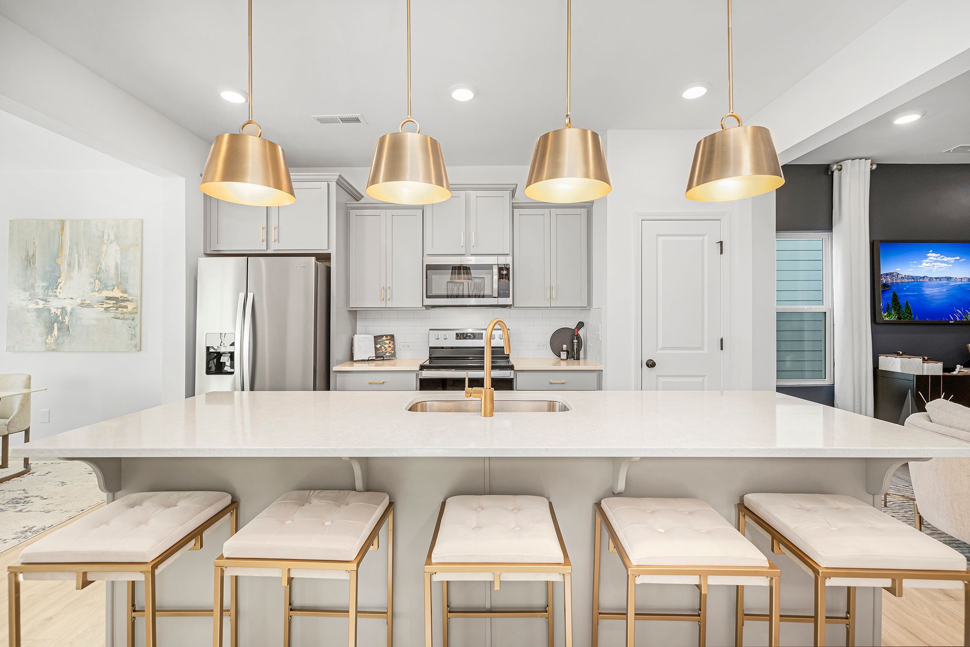 A kitchen with a large island , stools , a refrigerator and a television.