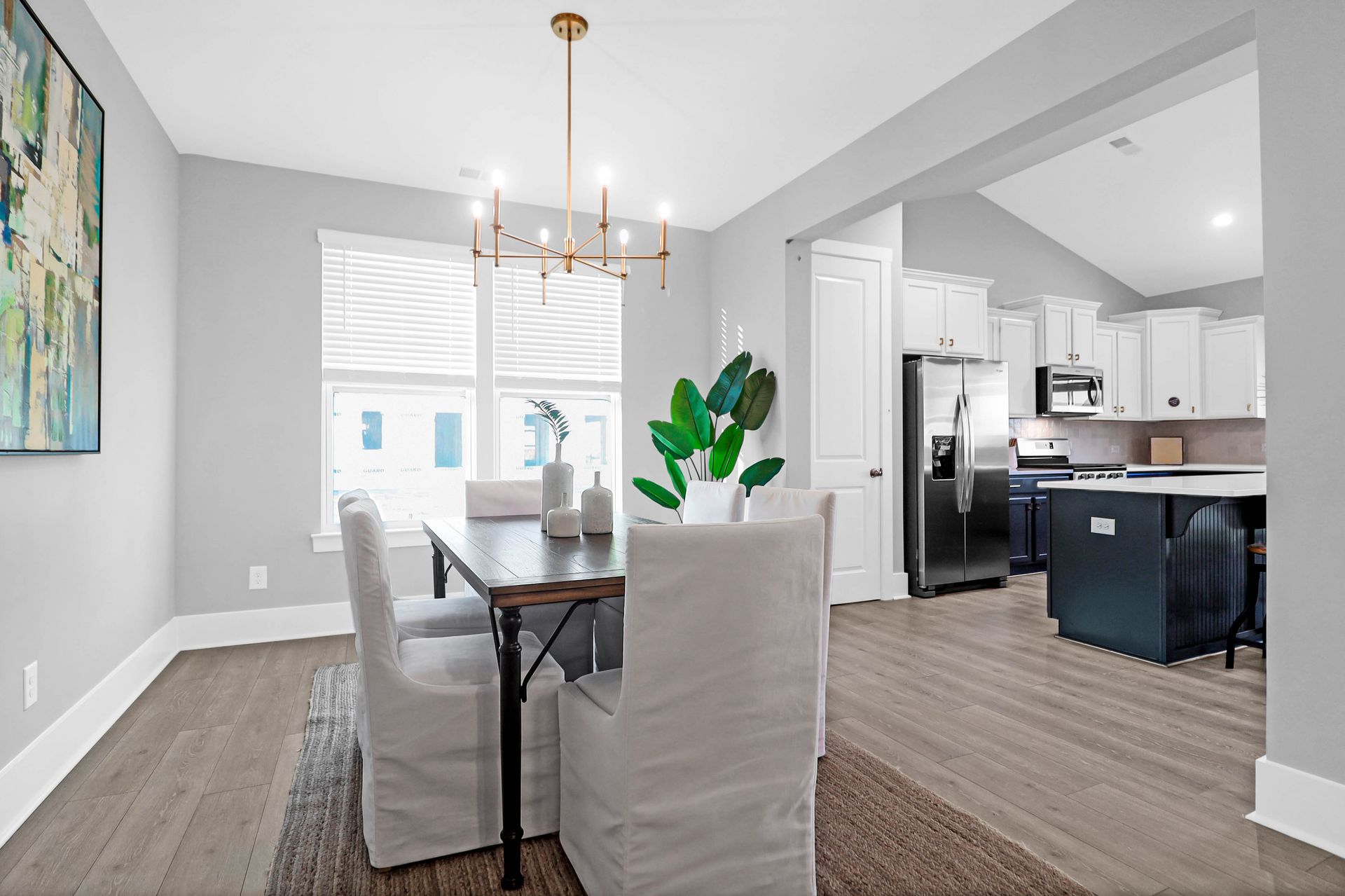 A dining room with a table and chairs and a kitchen in the background.
