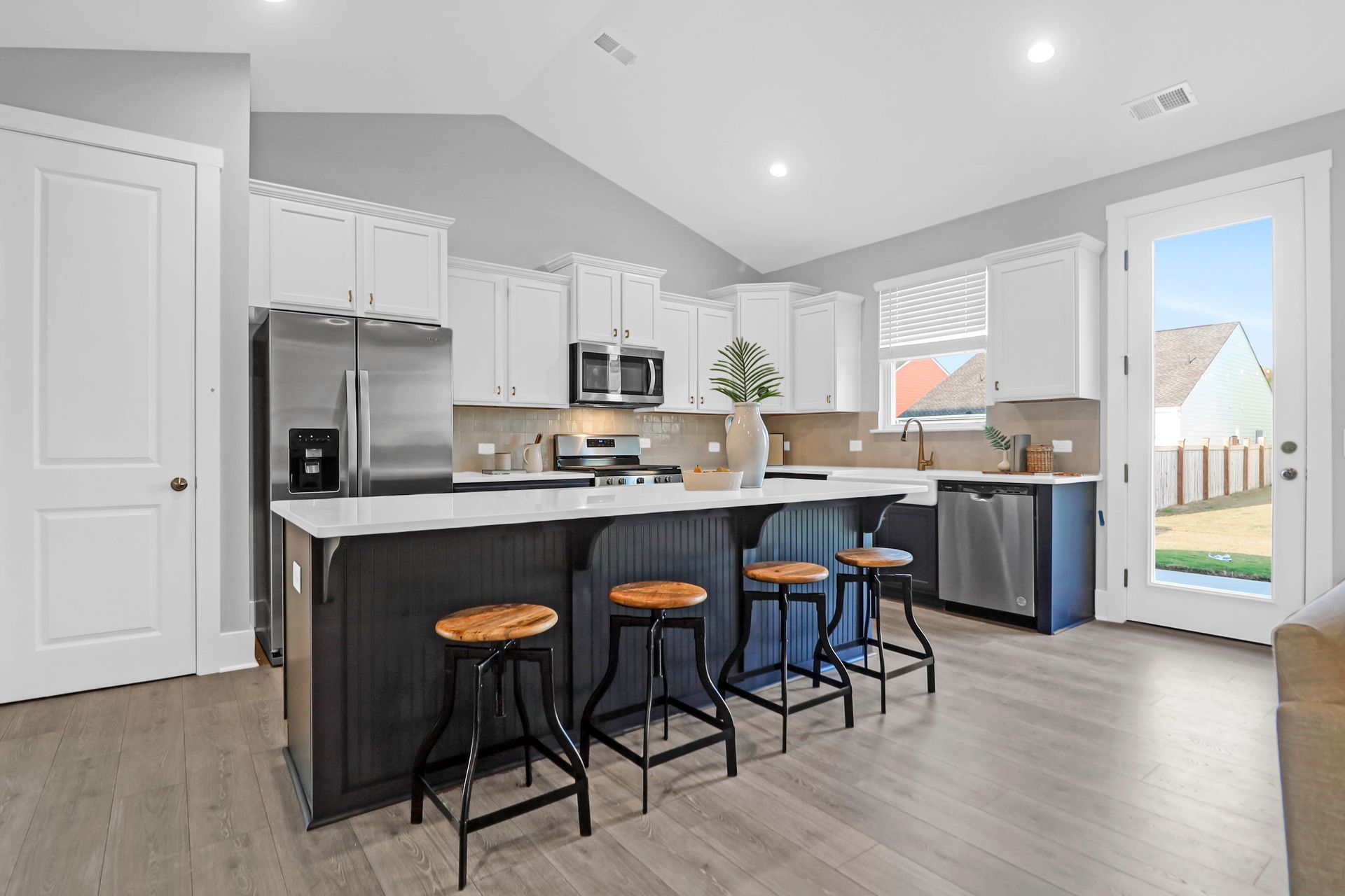 A kitchen with white cabinets , stainless steel appliances , a large island and stools.