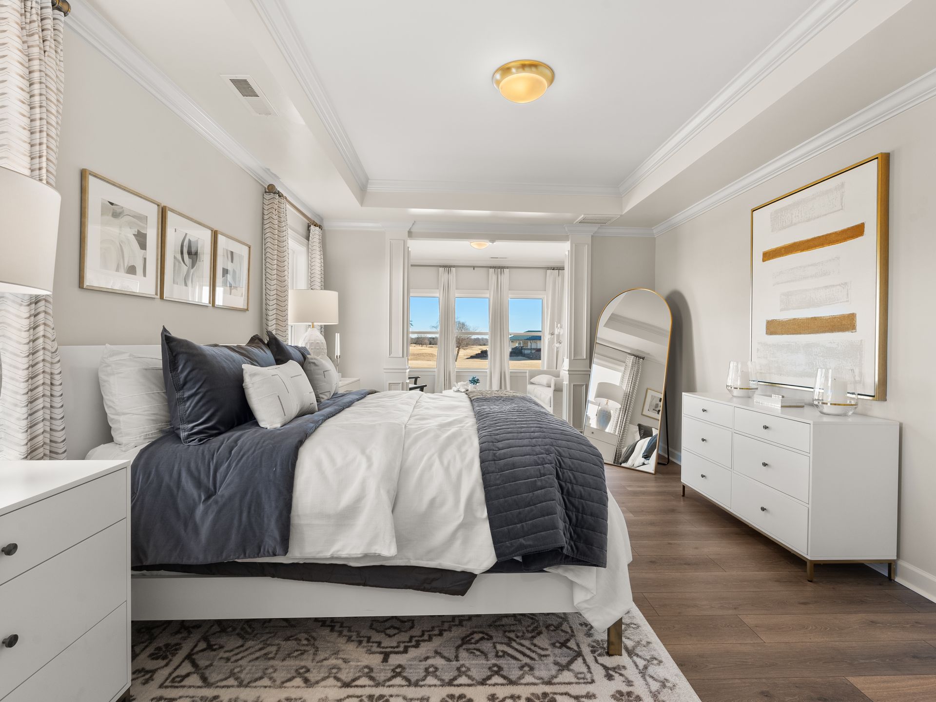 A bedroom with a large bed , dresser , nightstand and mirror.