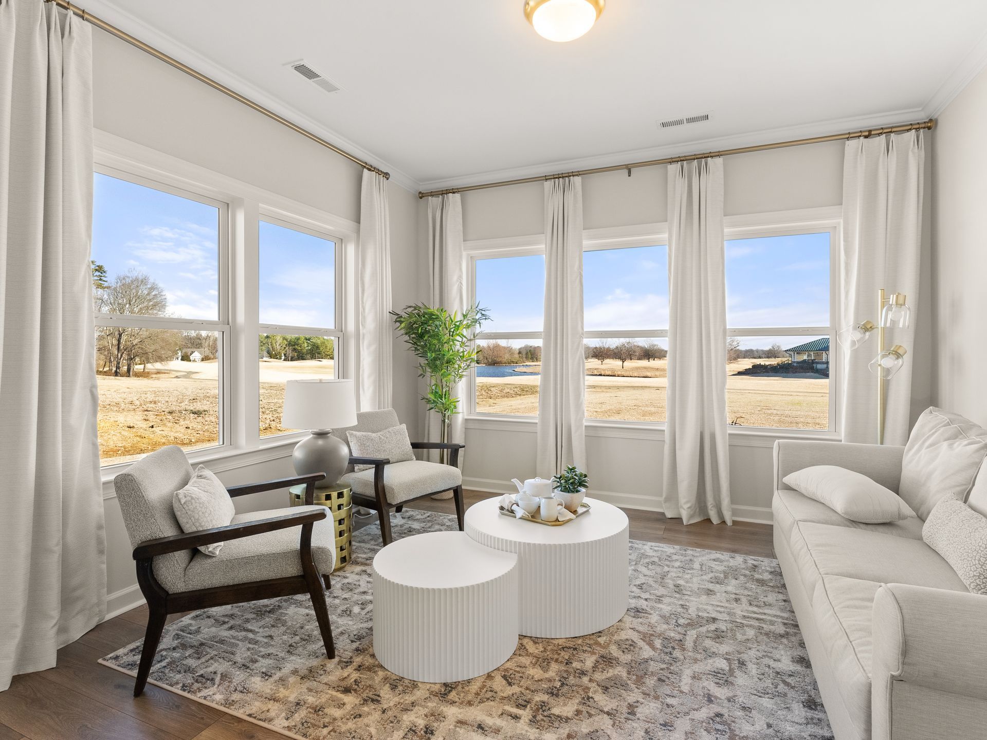 A living room with a couch , chairs , coffee tables and lots of windows.