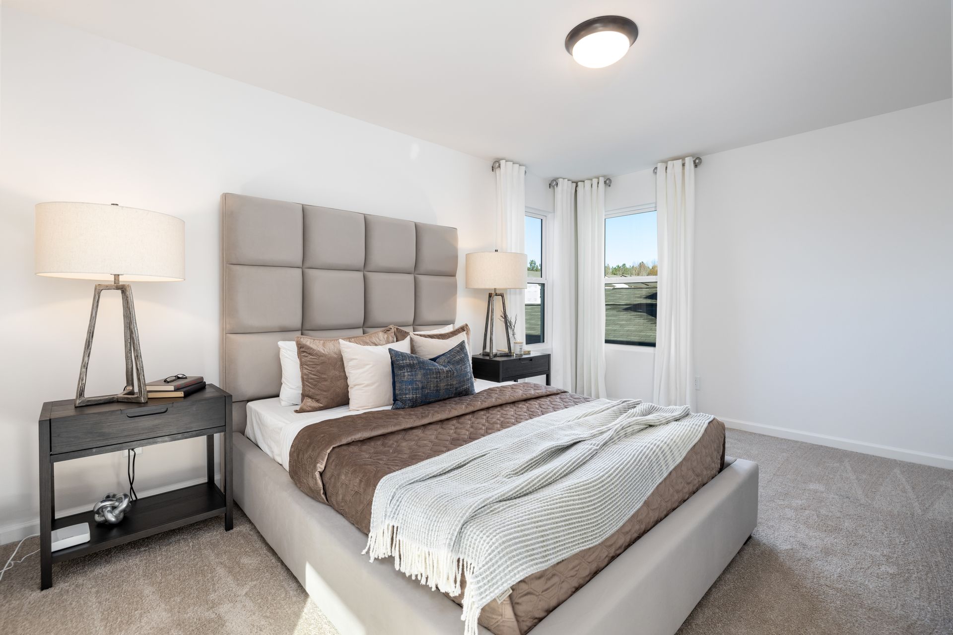 A bedroom with a bed , nightstand , lamp and window.