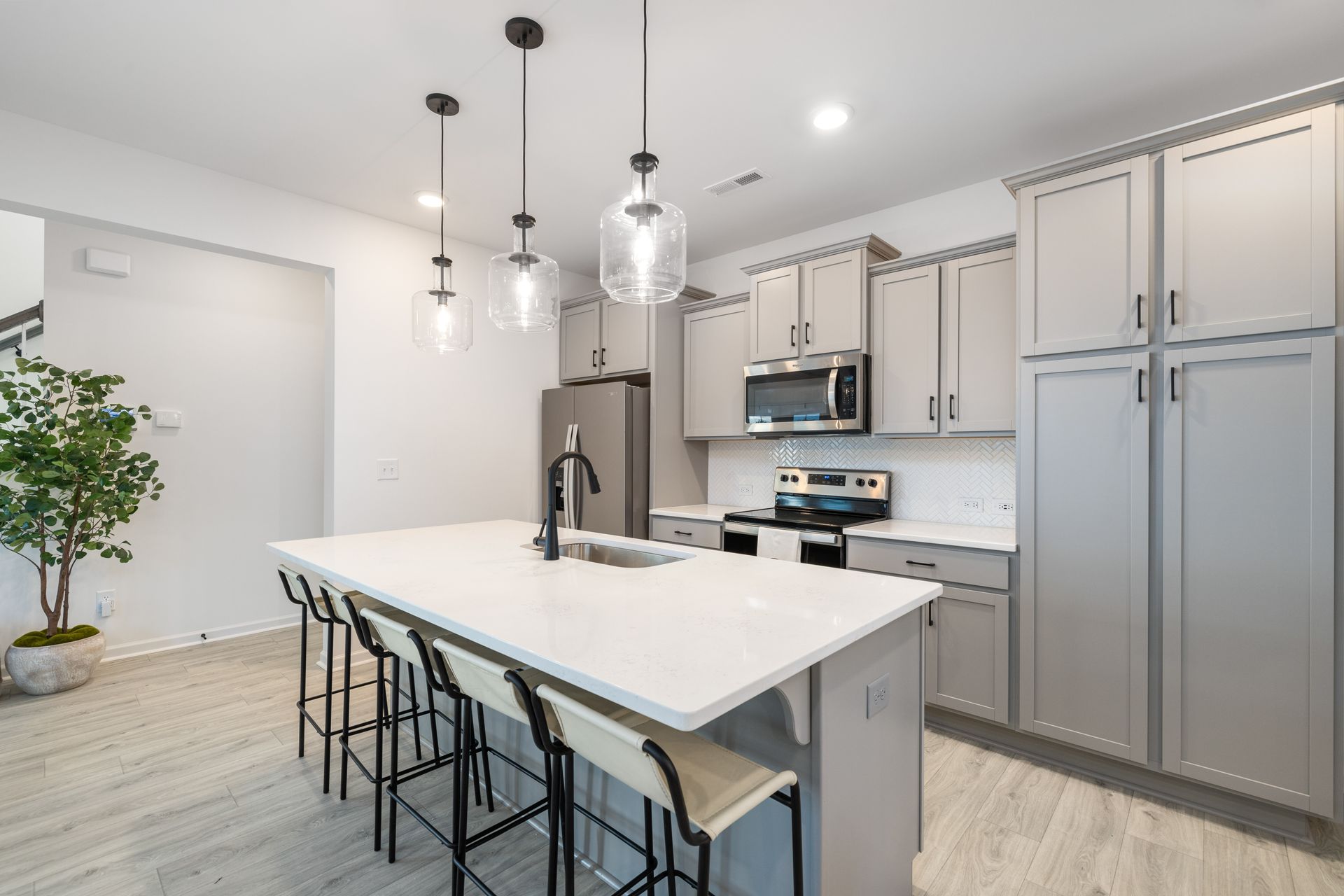 A kitchen with gray cabinets , white counter tops , stainless steel appliances and a large island.