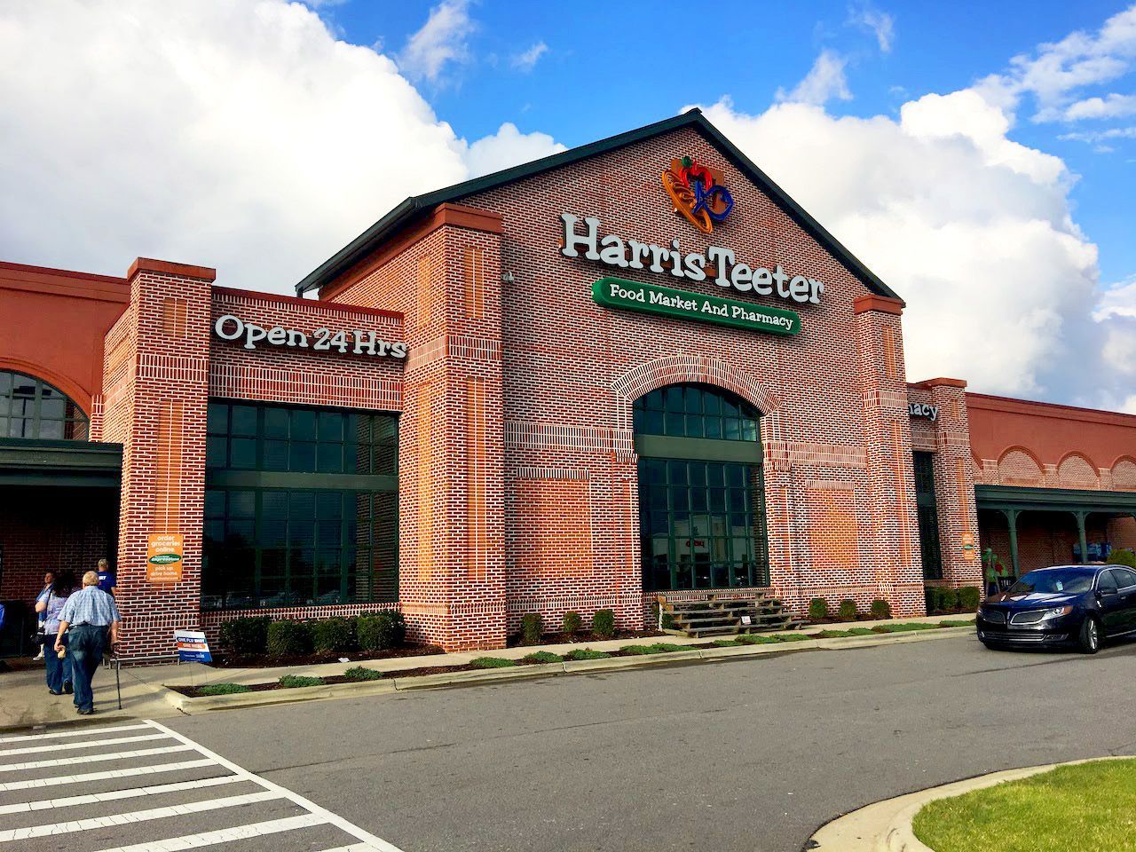 The front of a harris teeter grocery store with a car parked in front of it.