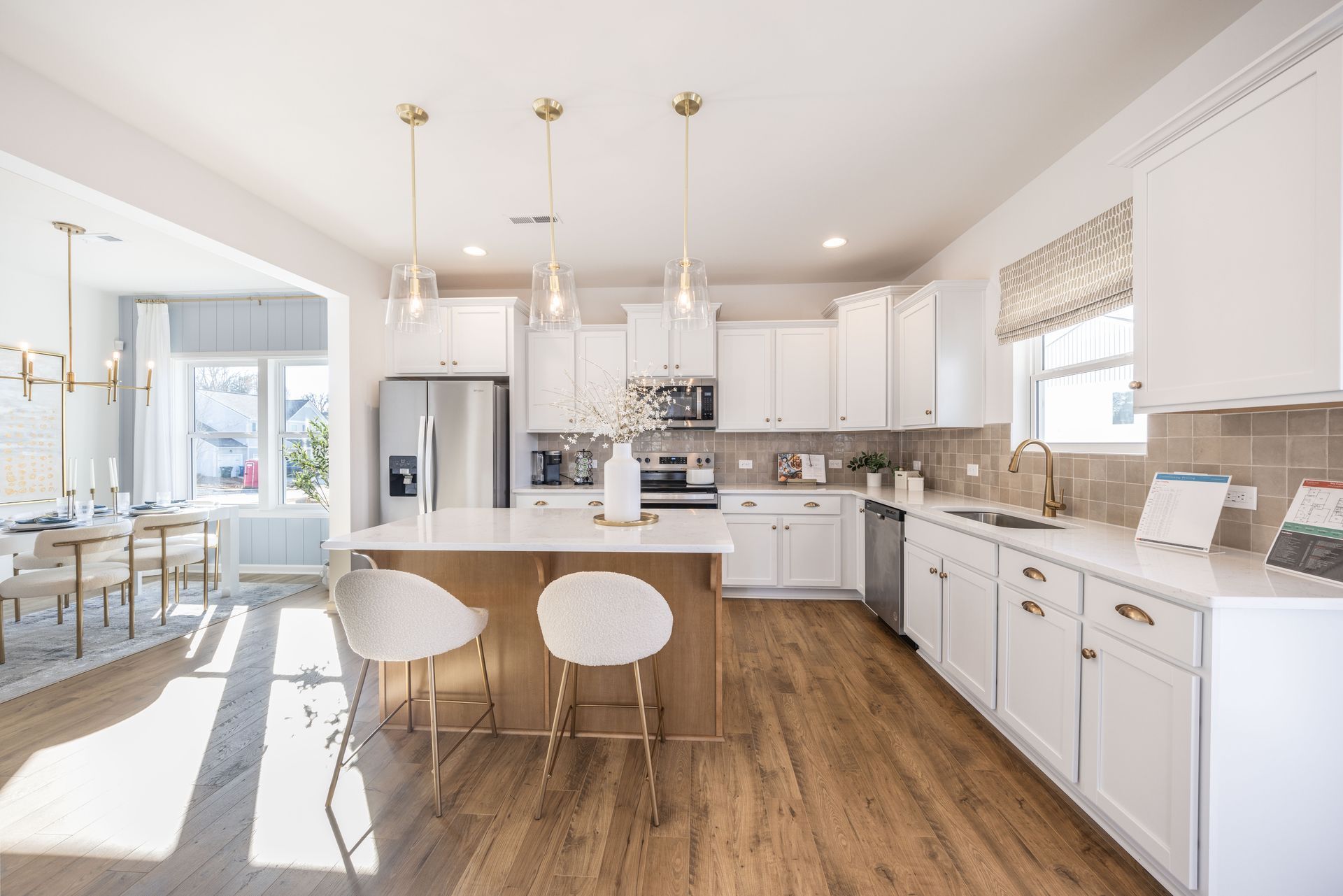 A kitchen with white cabinets , hardwood floors , stainless steel appliances and a large island.