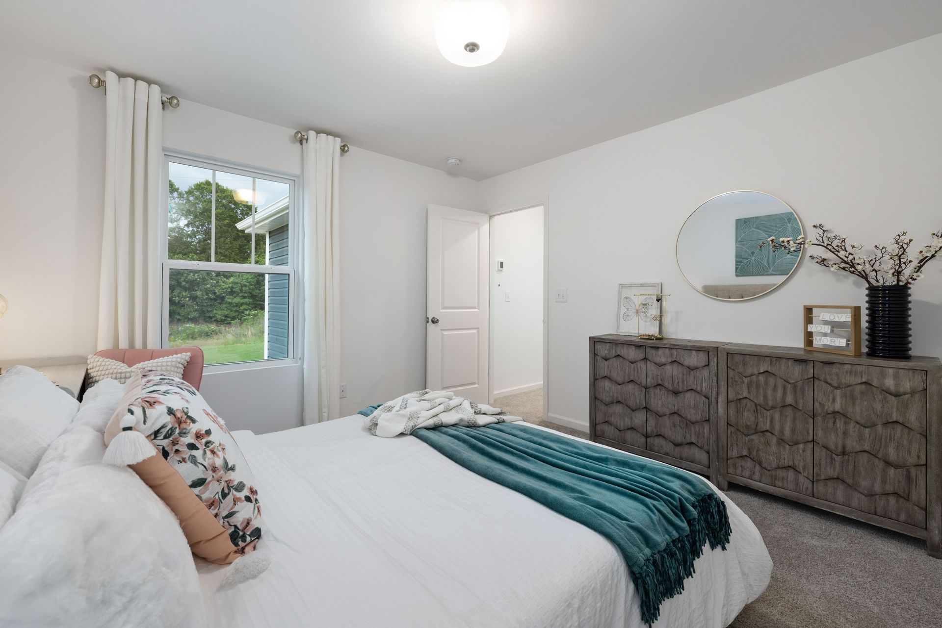 A bedroom with a bed , dresser , mirror and window.