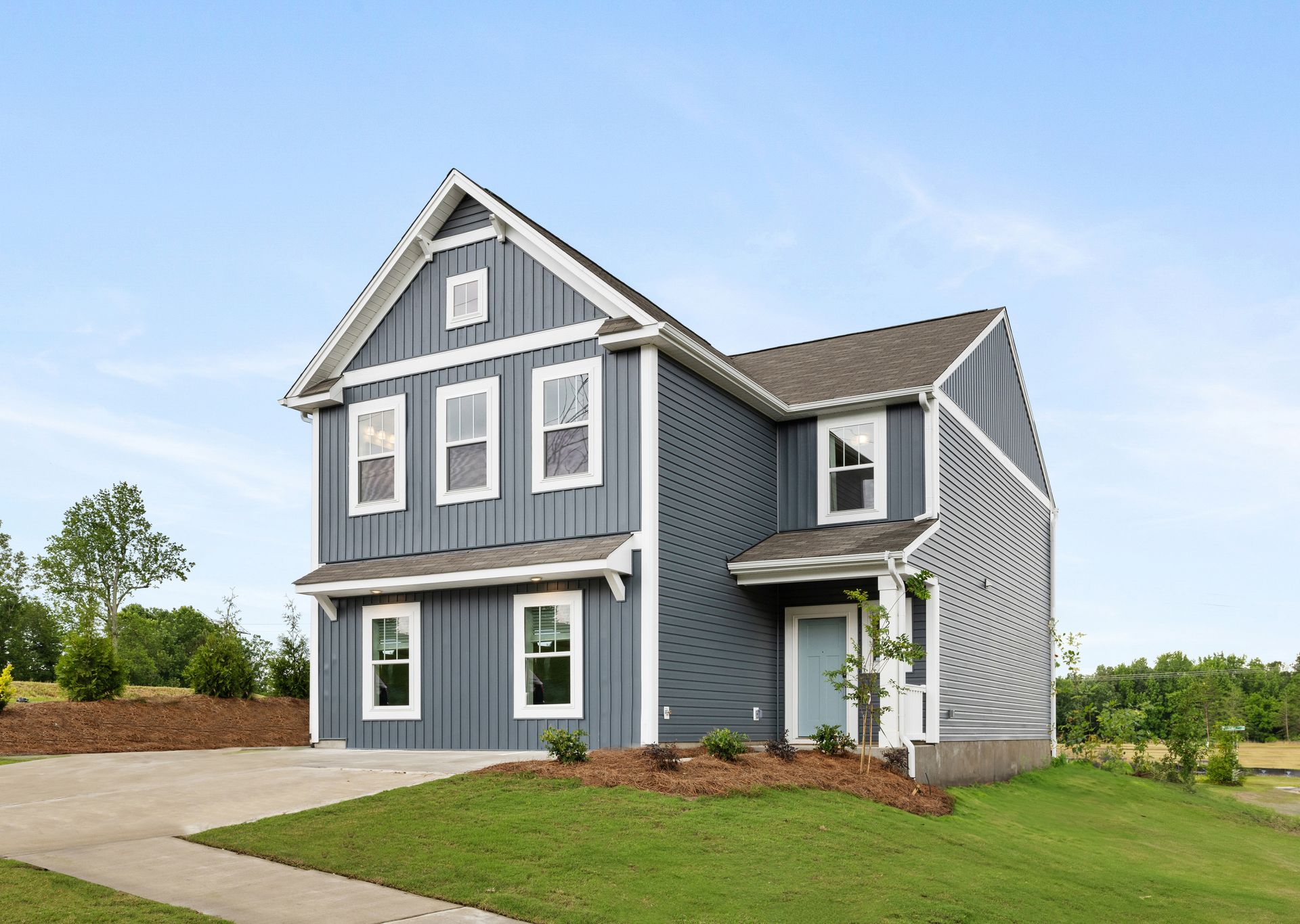 A large gray house with white trim is sitting on top of a lush green field.
