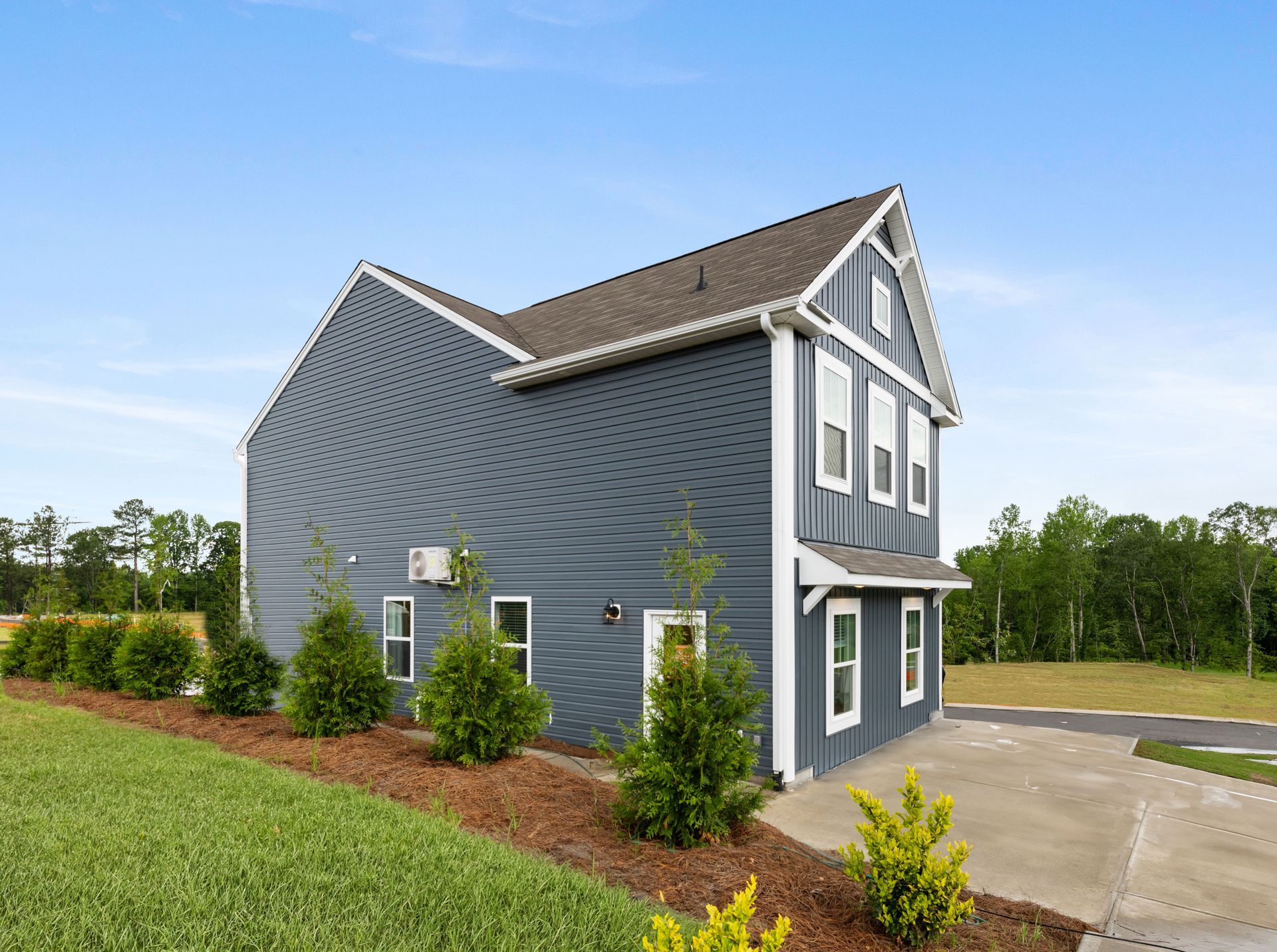 A large gray house with a garage and a driveway is sitting on top of a lush green field.