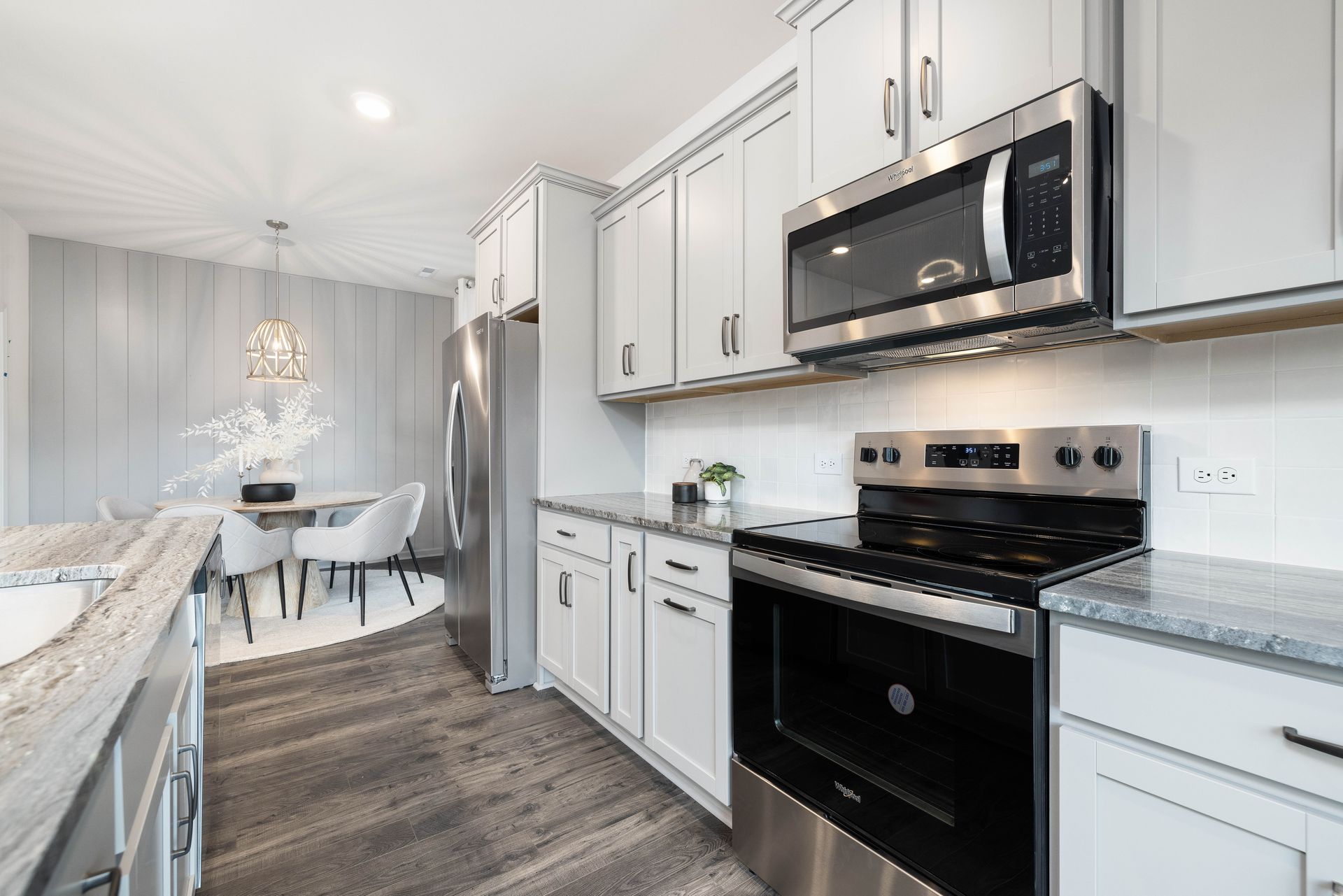 A kitchen with white cabinets , stainless steel appliances , a stove , microwave and refrigerator.
