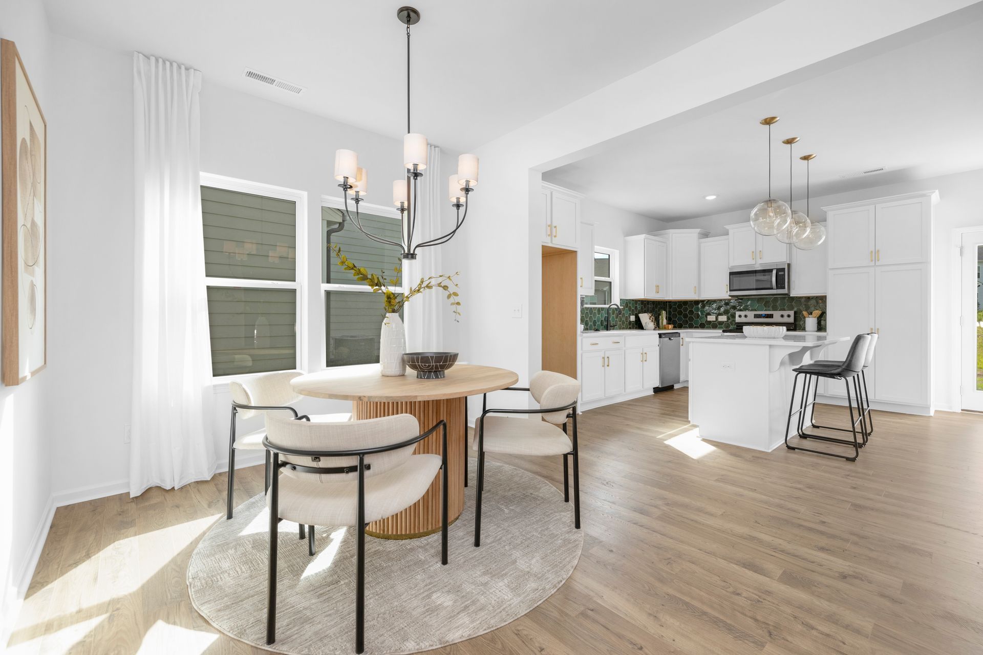 A dining room with a round wooden table and chairs, open to a white kitchen.
