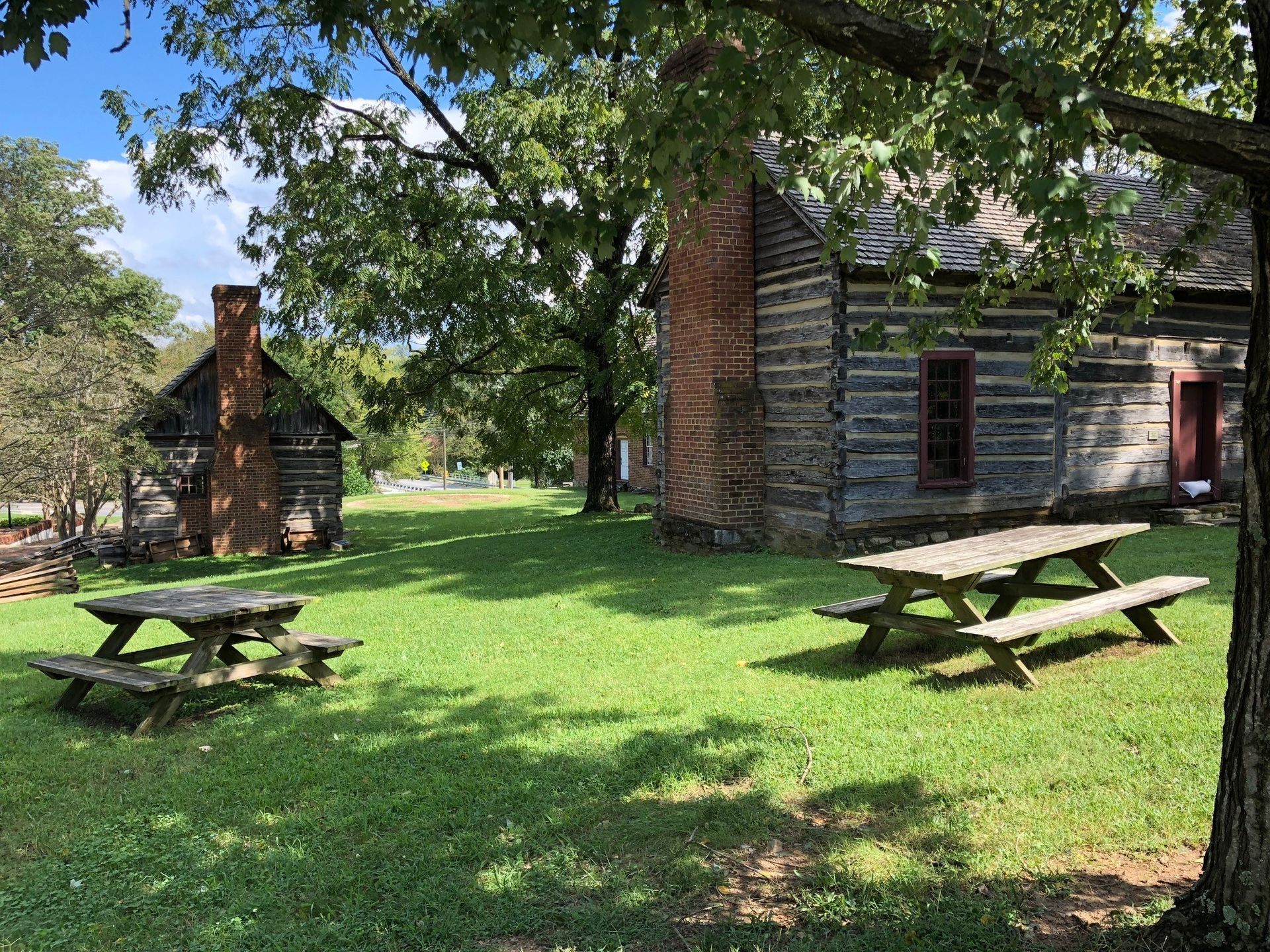 There are two picnic tables in the grass in front of a log cabin.