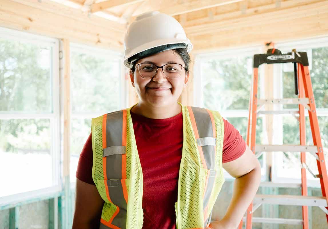 Woman in hard hat and safety vest smiling at construction site.