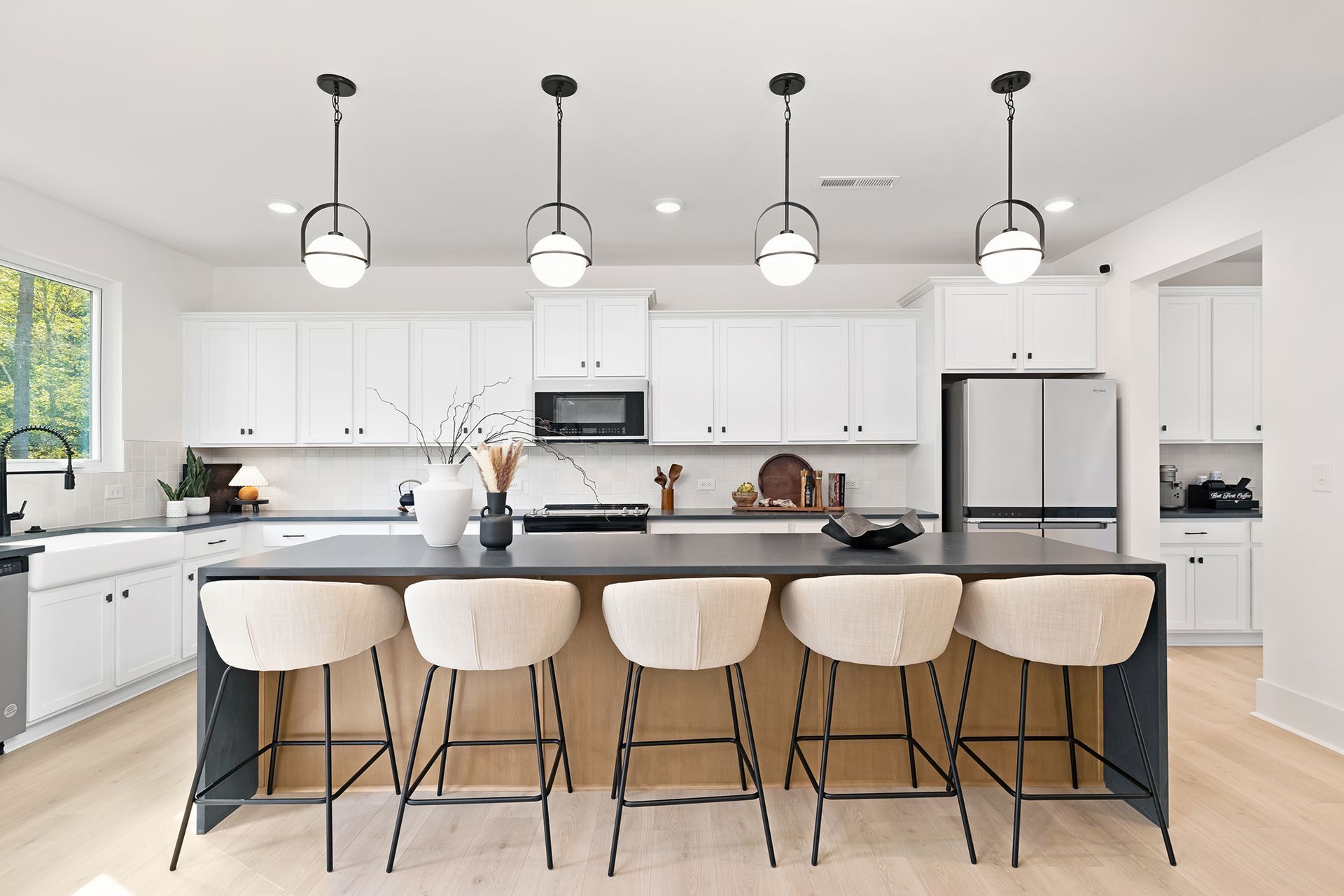 A kitchen with white cabinets , a large island , stools and a refrigerator.