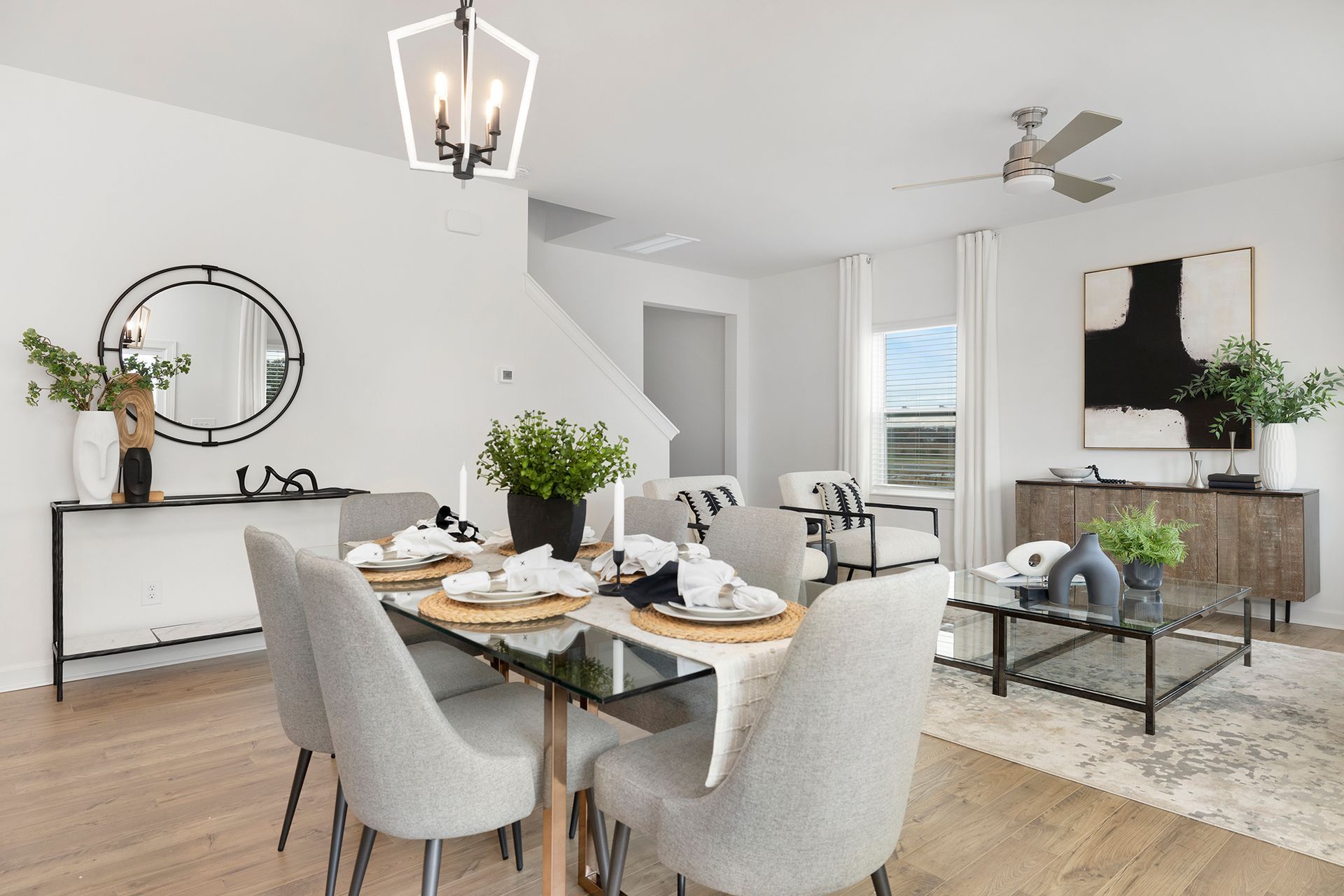 A dining room with a table and chairs and a living room with a ceiling fan.