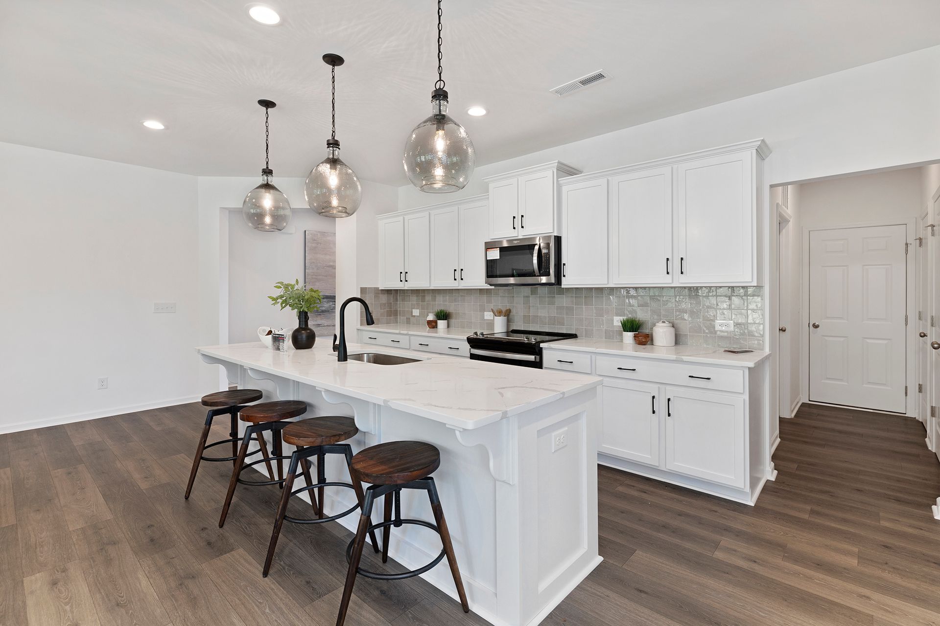 A kitchen with white cabinets and a large island with stools.