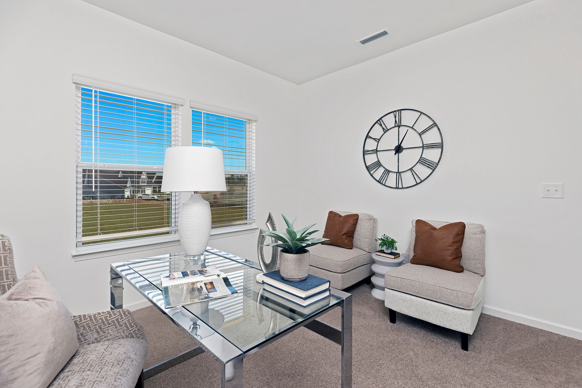 A living room with a desk , chairs and a clock on the wall.