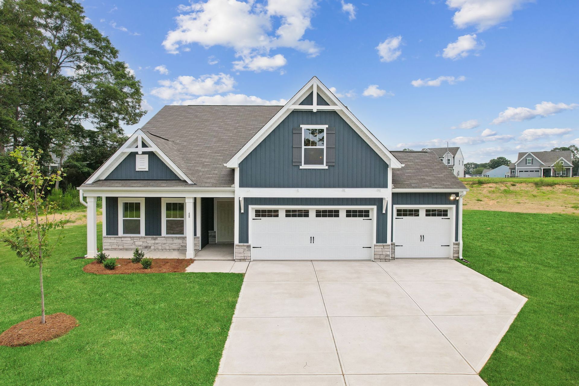 A blue house with a white garage door is sitting on top of a lush green field.