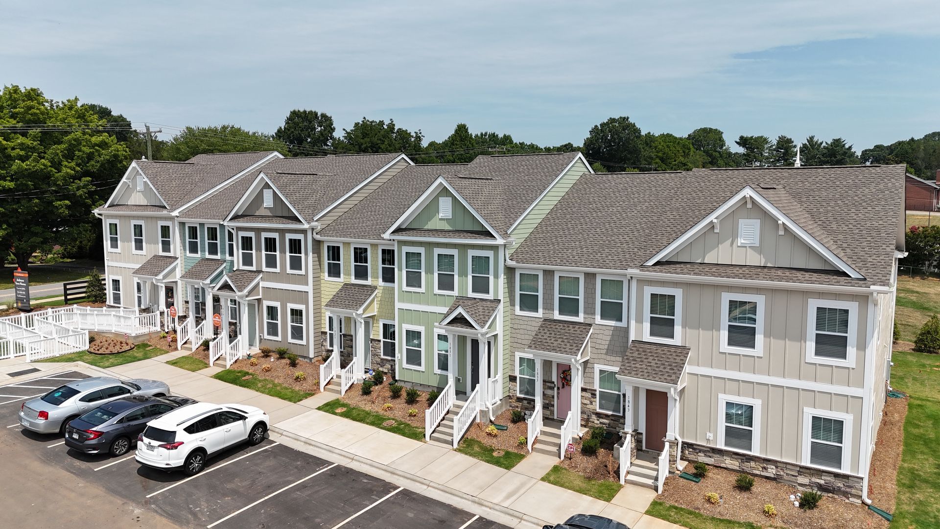 Row of colorful townhouses with cars parked in front; blue sky background.
