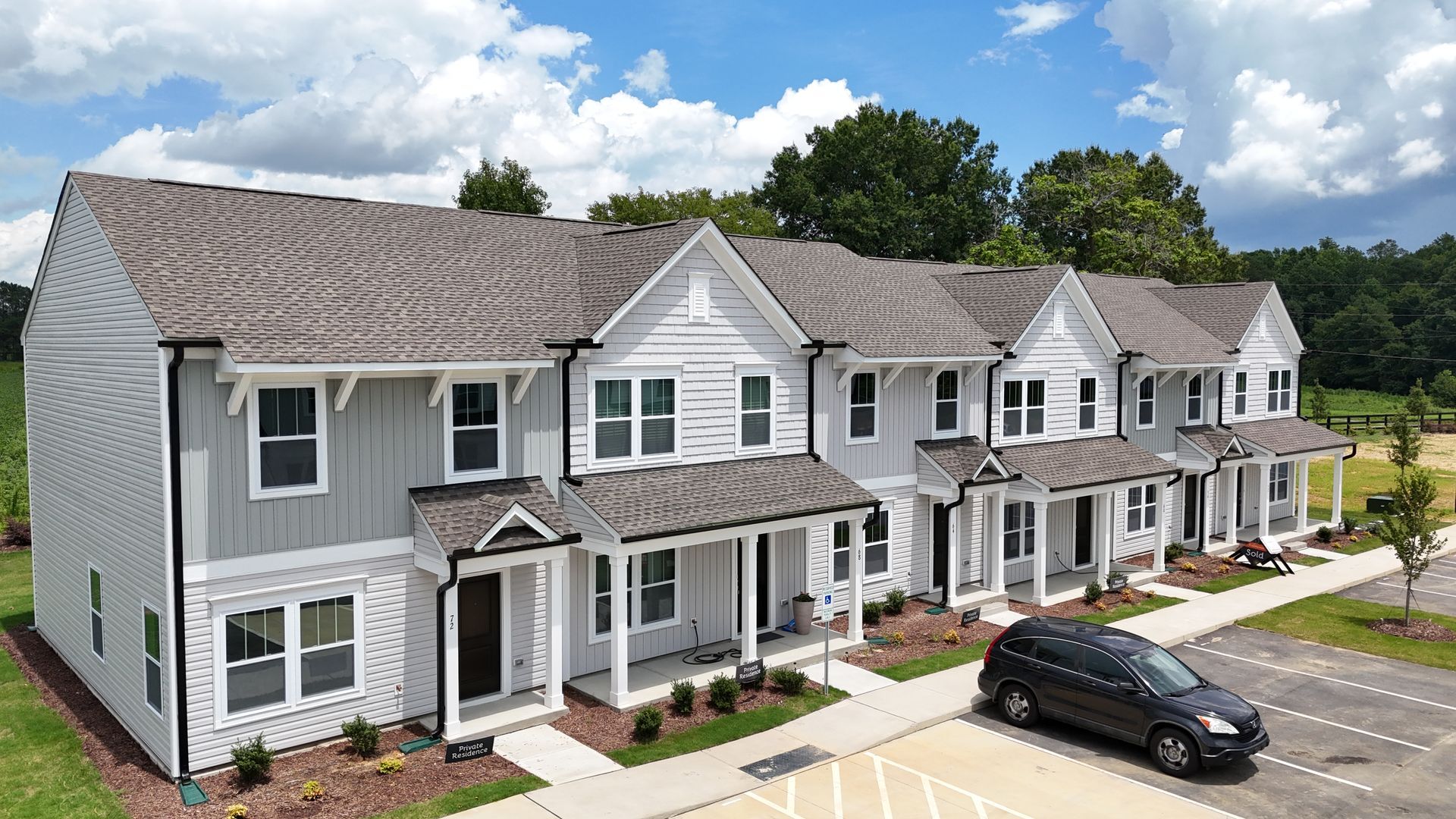 Row of modern townhomes with gray siding, white trim, and a black car parked in front.