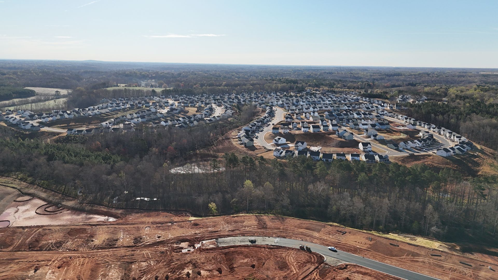 Aerial view of a residential development nestled in a wooded area, with construction in foreground and blue sky.