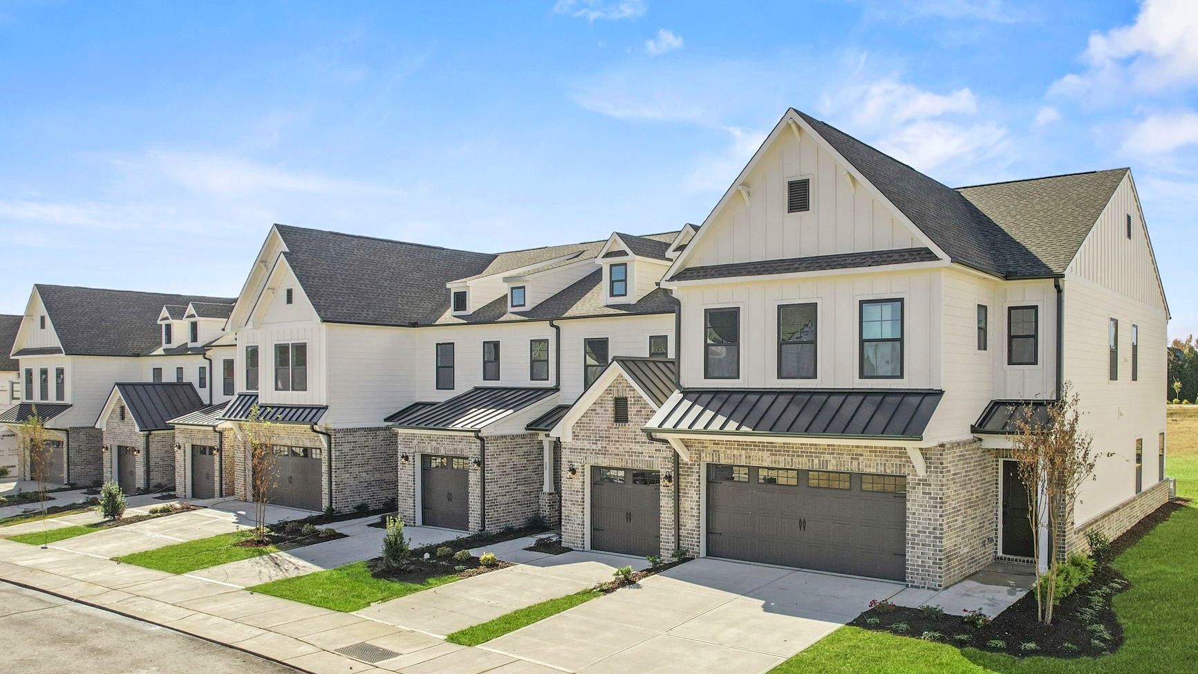 Row of modern townhouses with white siding, gray roofs, and stone accents under a blue sky.