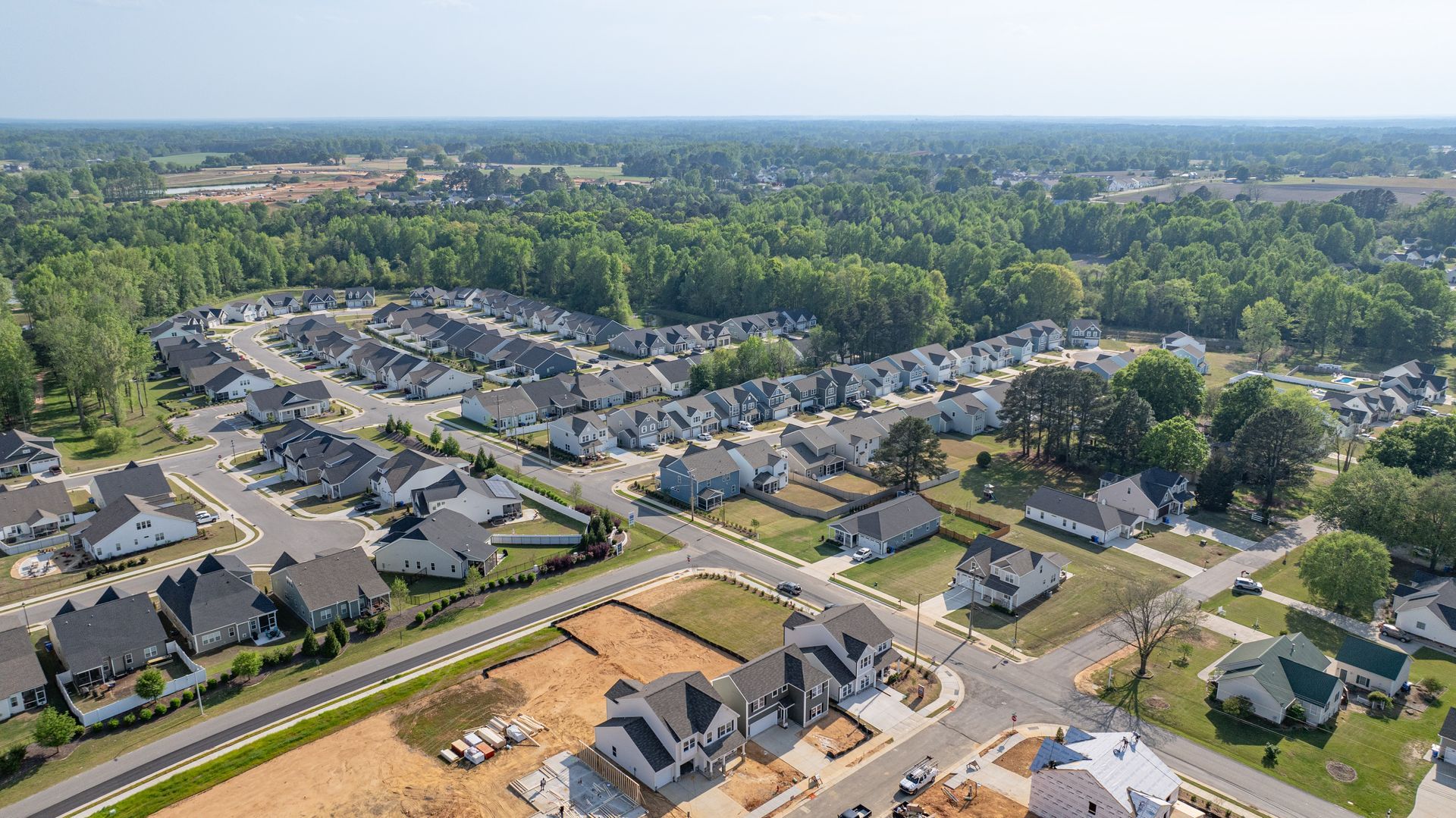 Aerial view of a suburban neighborhood with rows of houses surrounded by trees, clear sky.