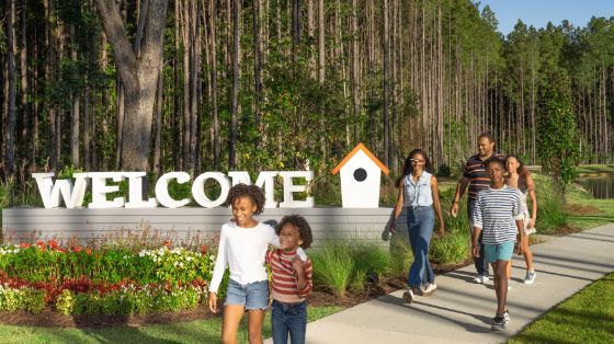 a family is walking down a sidewalk in front of a welcome sign .