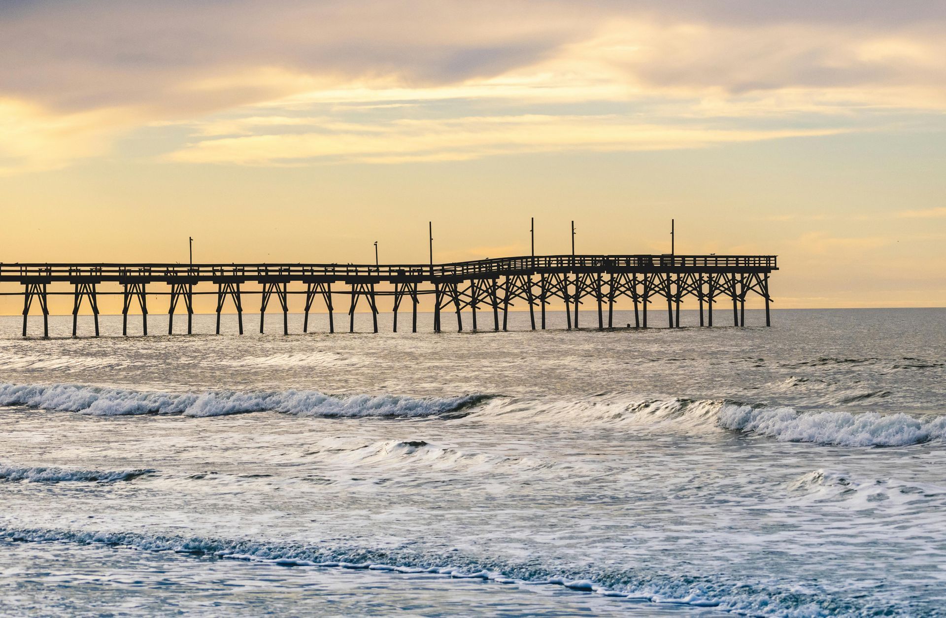 A pier in the middle of the ocean at sunset.