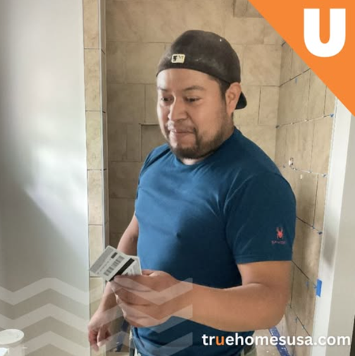 Man in blue shirt holding a card in a tiled bathroom.