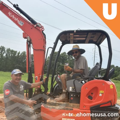 Two men near orange Kubota excavator; one operating, one posing. Cloudy day, green field.