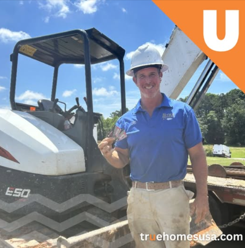 Man in hard hat with excavator, smiles, outdoors.