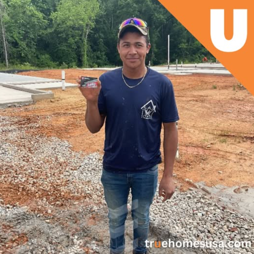 Man in blue shirt and jeans holding keys, standing on a construction site. Orange 