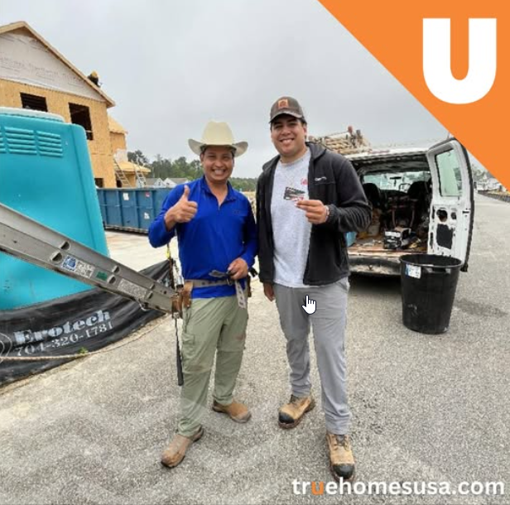 Two men pose at a construction site. One gives a thumbs up. Both are smiling. Blue, white, and brown tones.