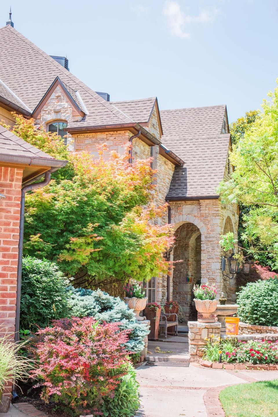 A large brick house surrounded by trees and bushes on a sunny day.