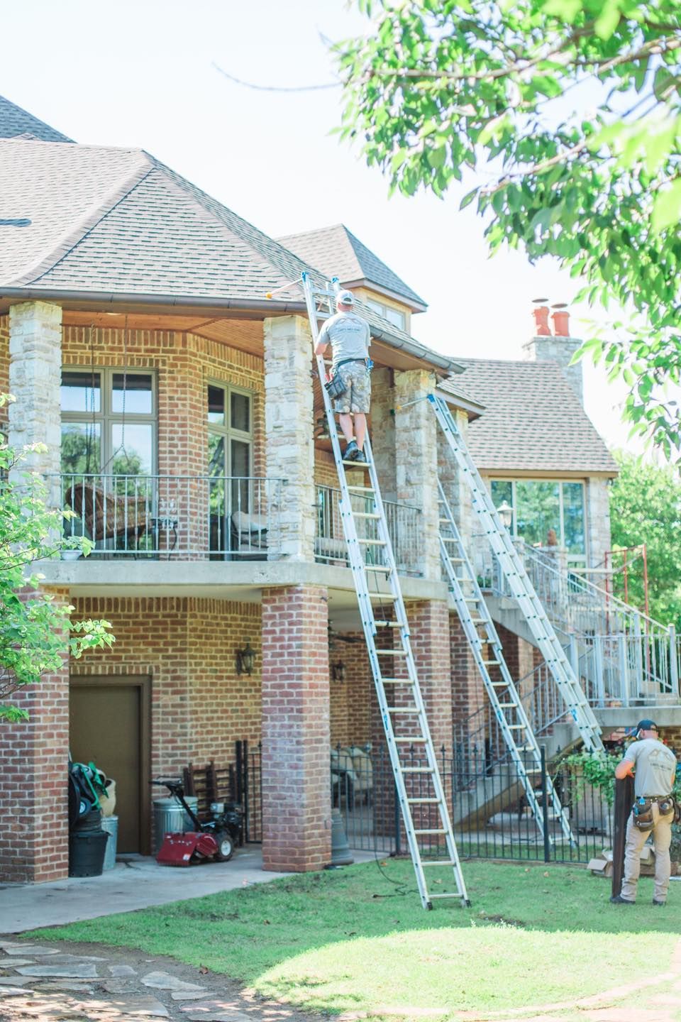 A man is standing on a ladder painting the roof of a house.