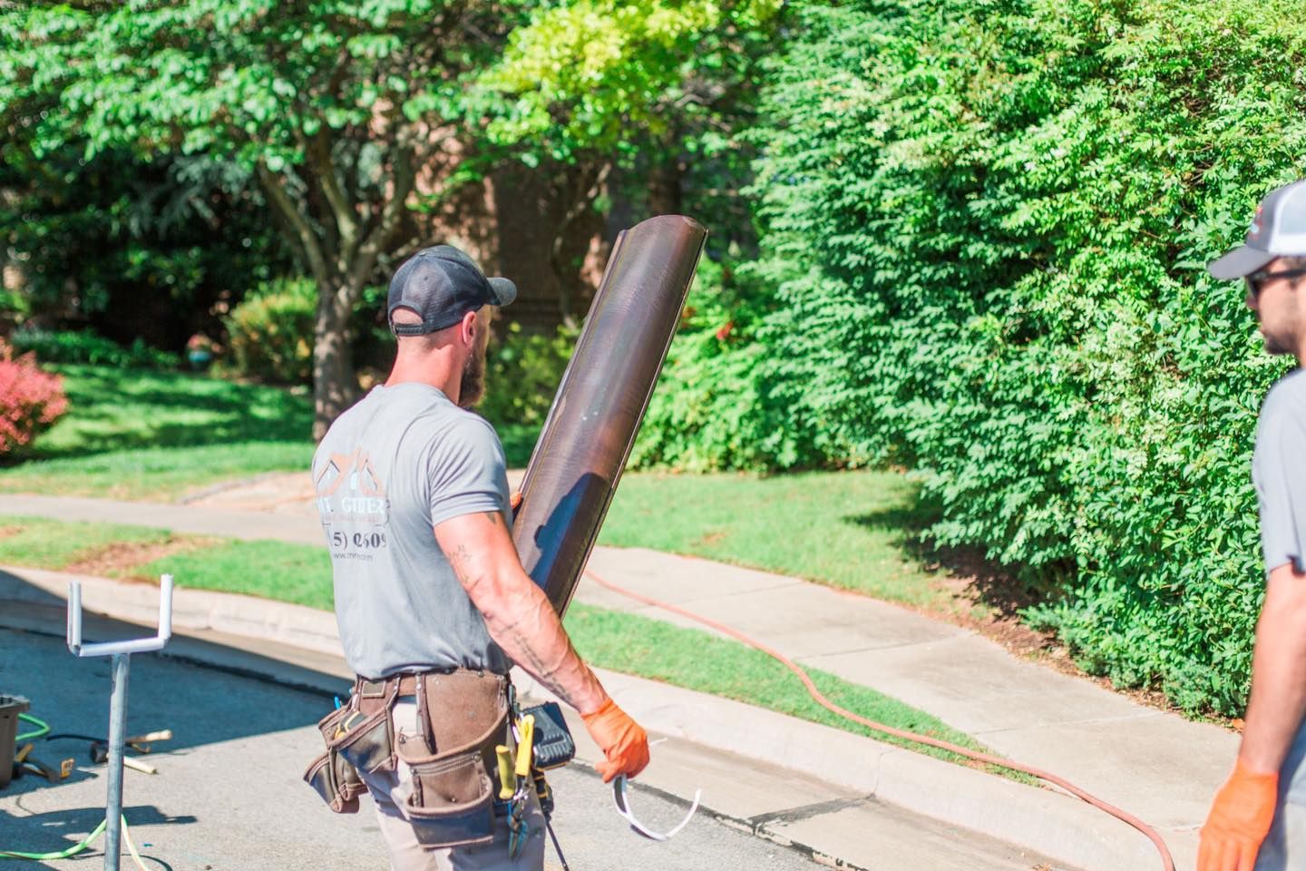 Two men are standing on a sidewalk holding a pipe.