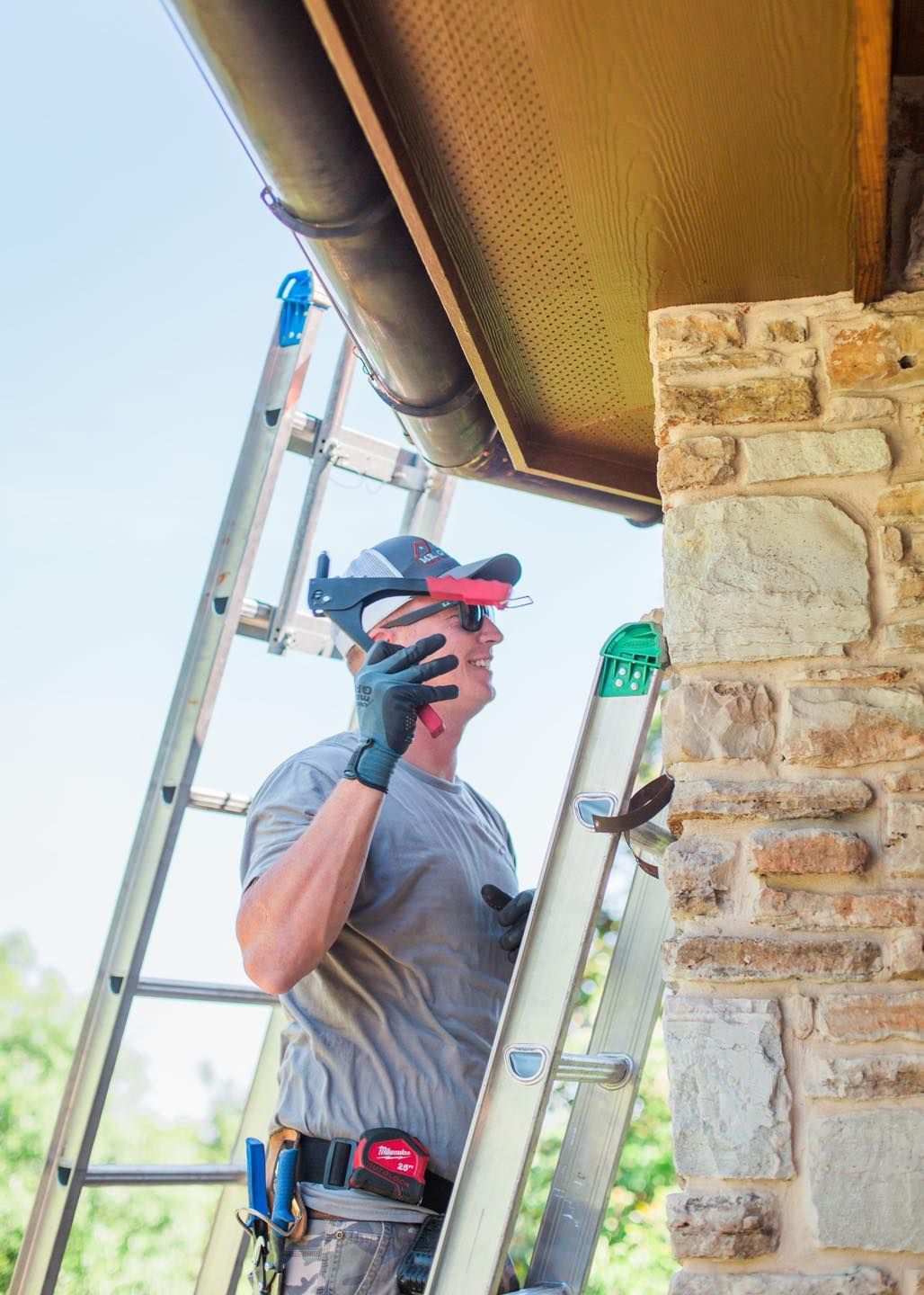 A man is standing on a ladder talking on a cell phone.