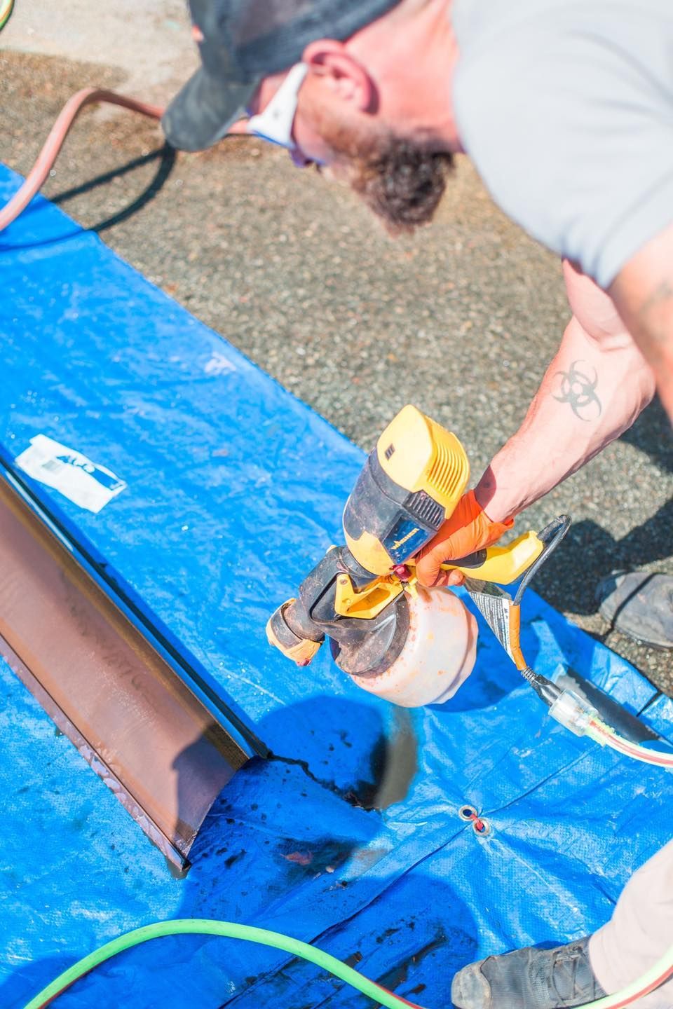 A man is spray painting a piece of wood on a blue tarp.