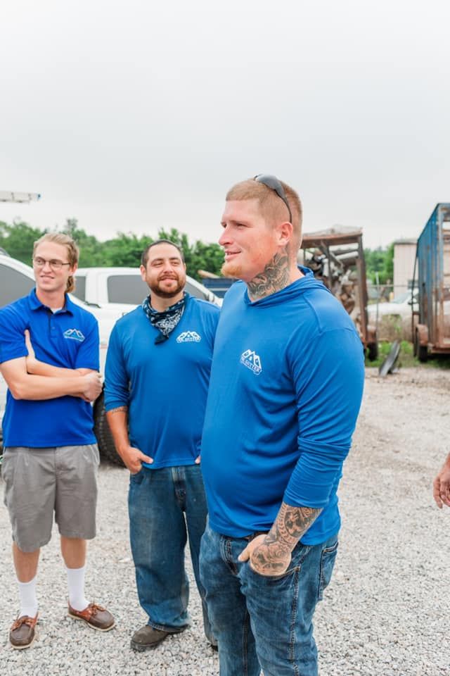 A group of men in blue shirts are standing in a gravel lot.