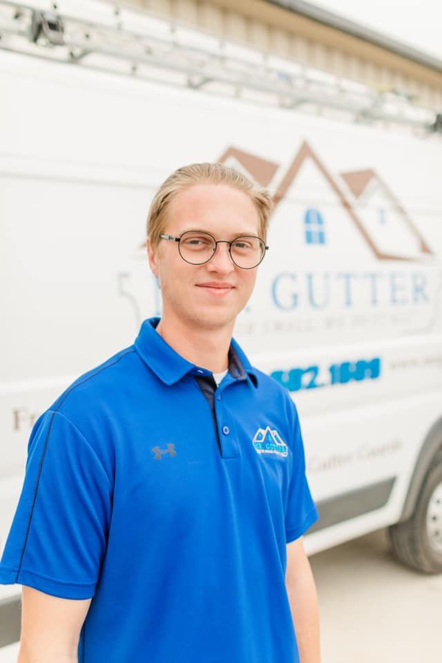A young man wearing glasses and a blue shirt is standing in front of a white van.