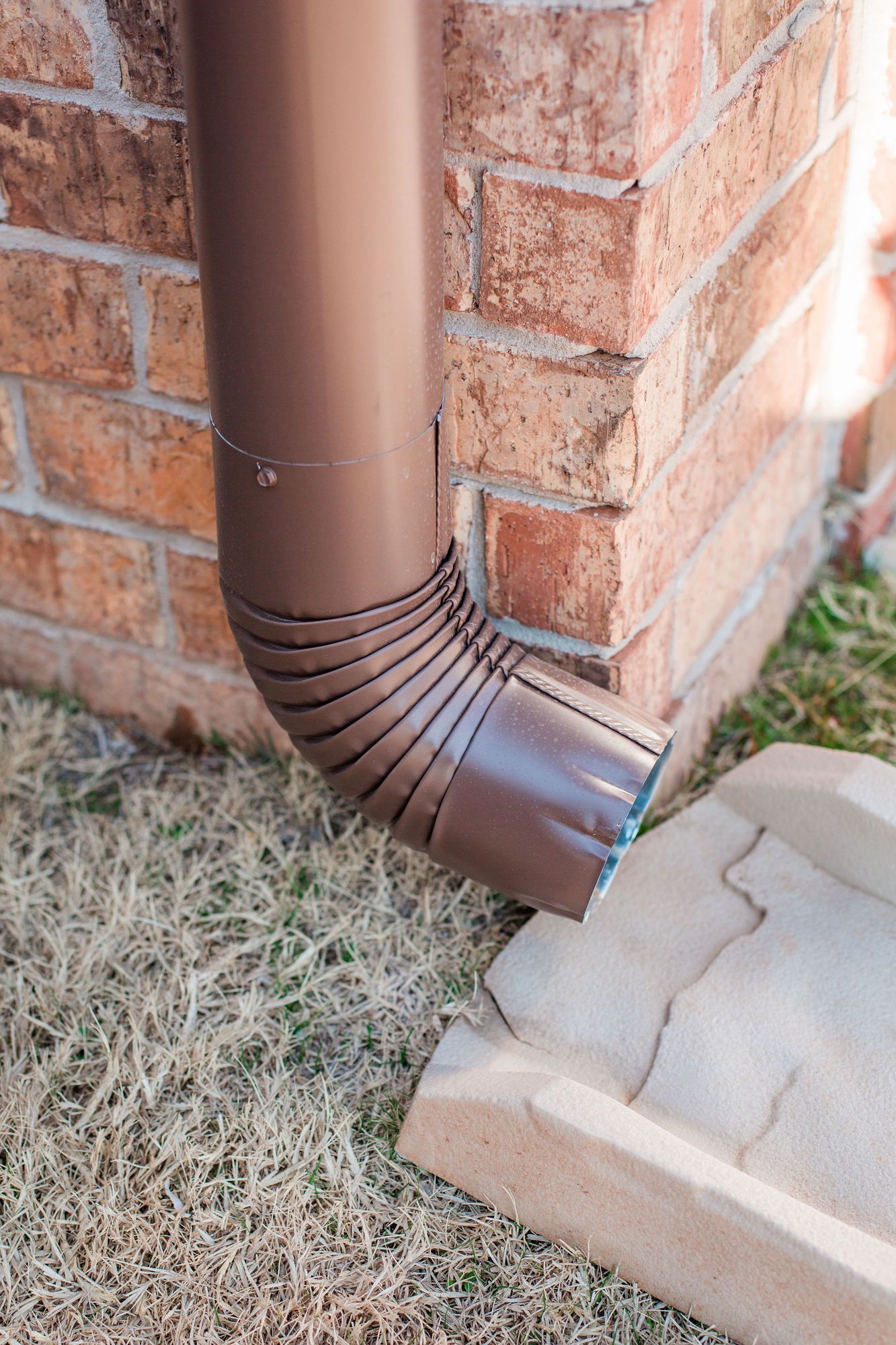 A brown rain gutter is attached to the side of a brick building.