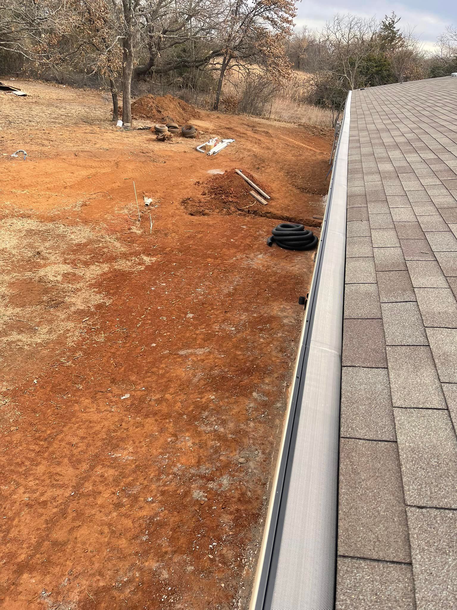 A gutter is sitting on top of a roof next to a dirt field.