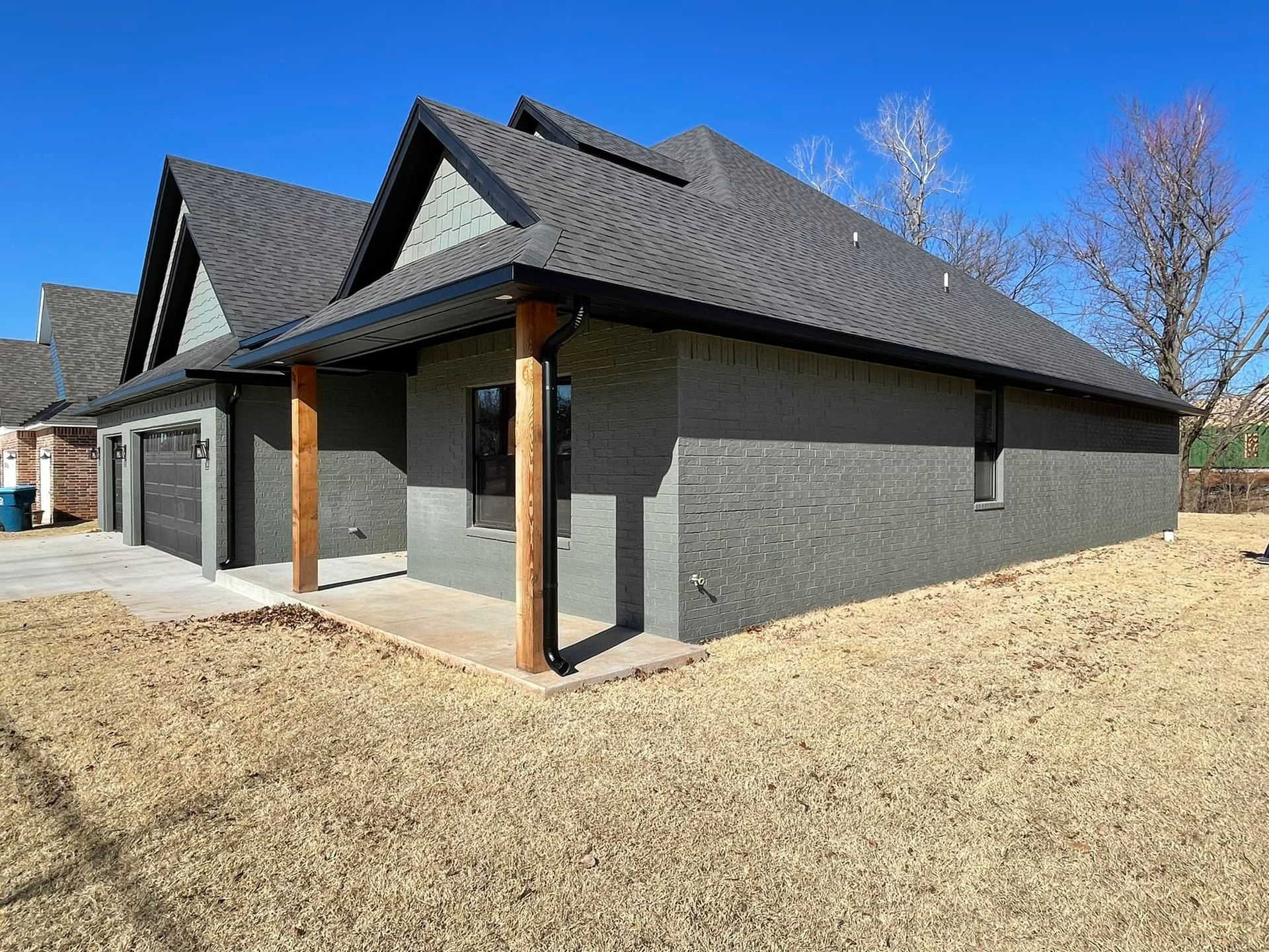 A large brick house with a gray roof is sitting in the middle of a grassy field.