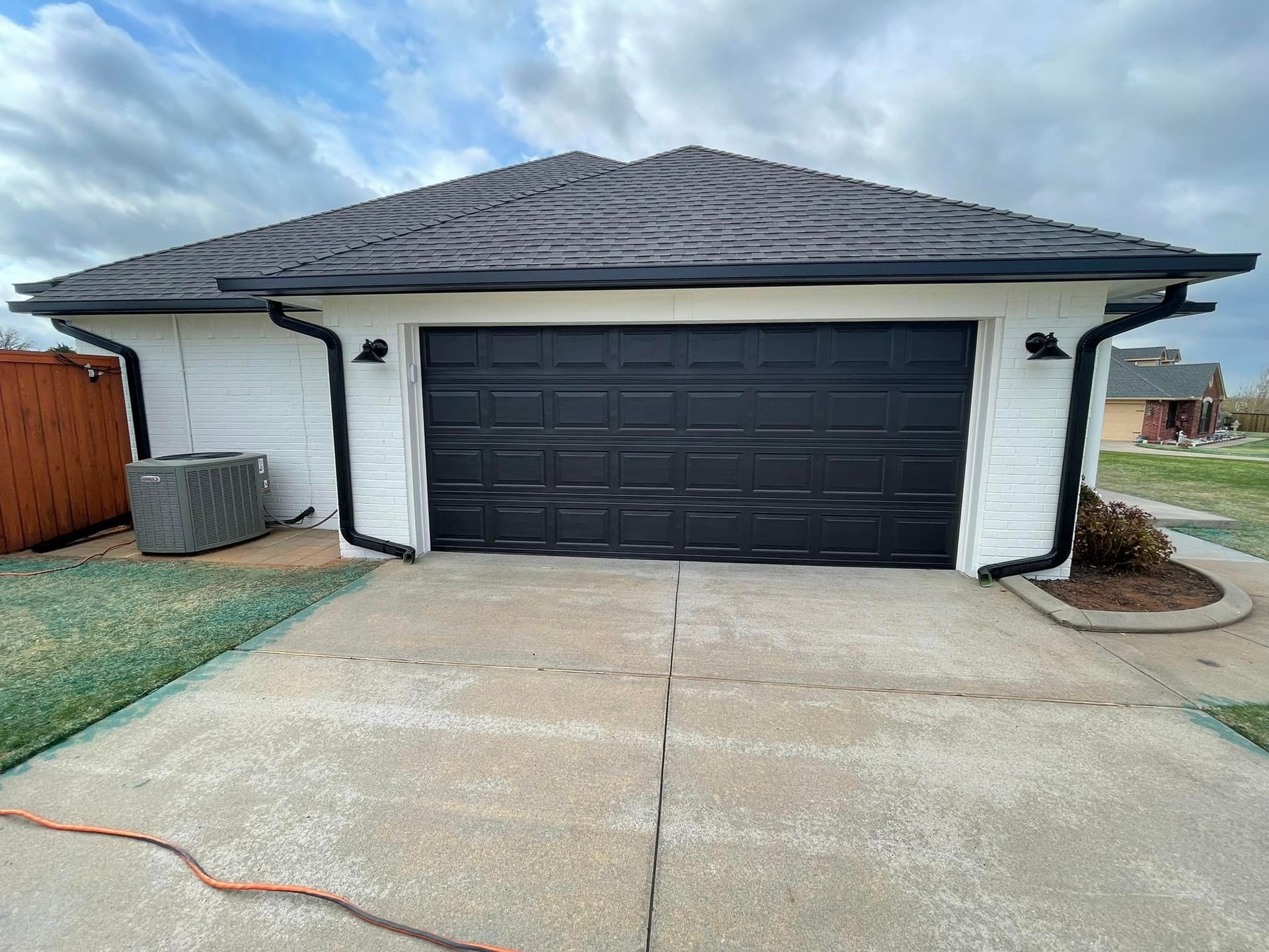 A white house with a black garage door and a black roof.