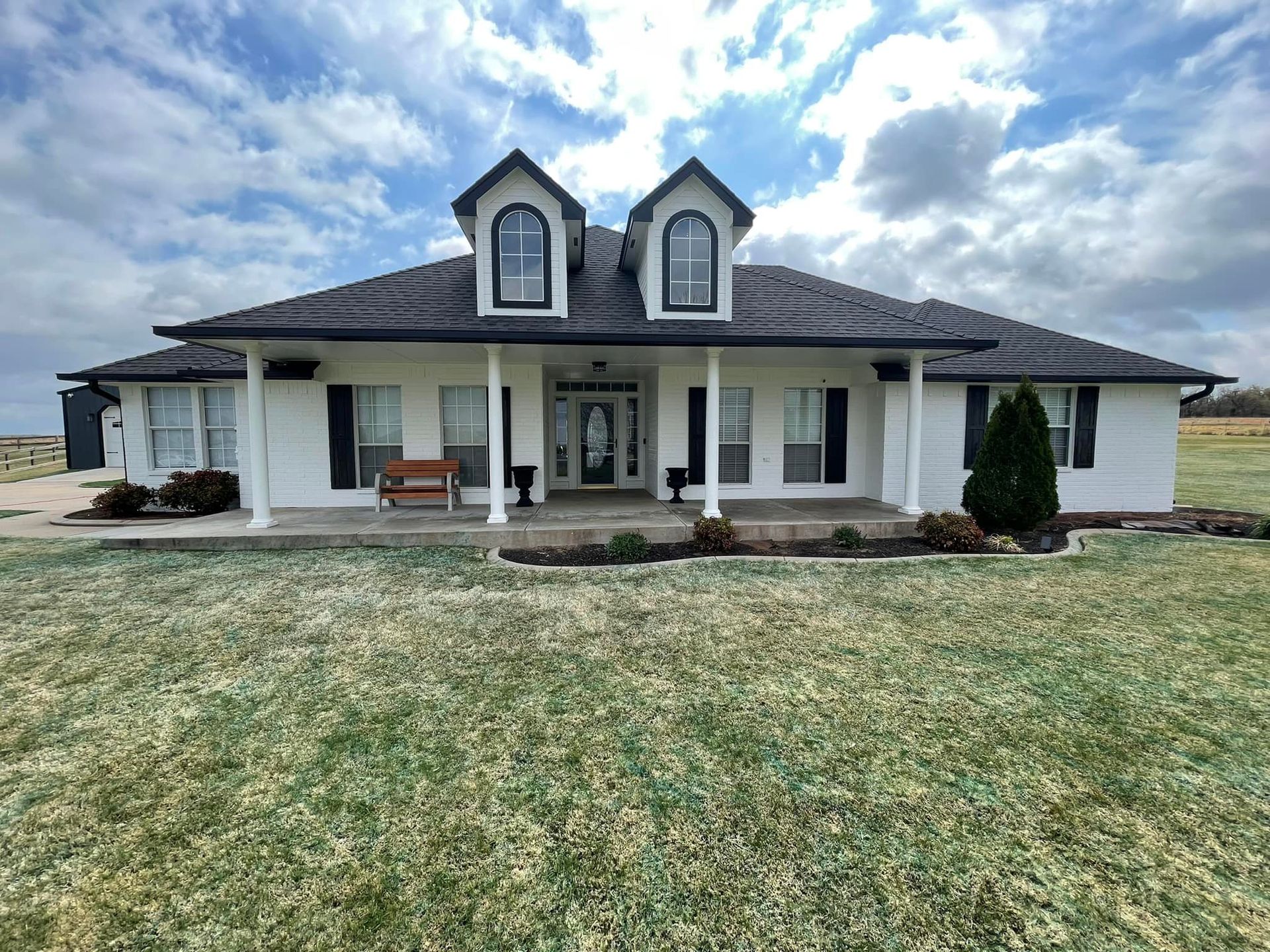 A large white house with a black roof is sitting on top of a lush green field.